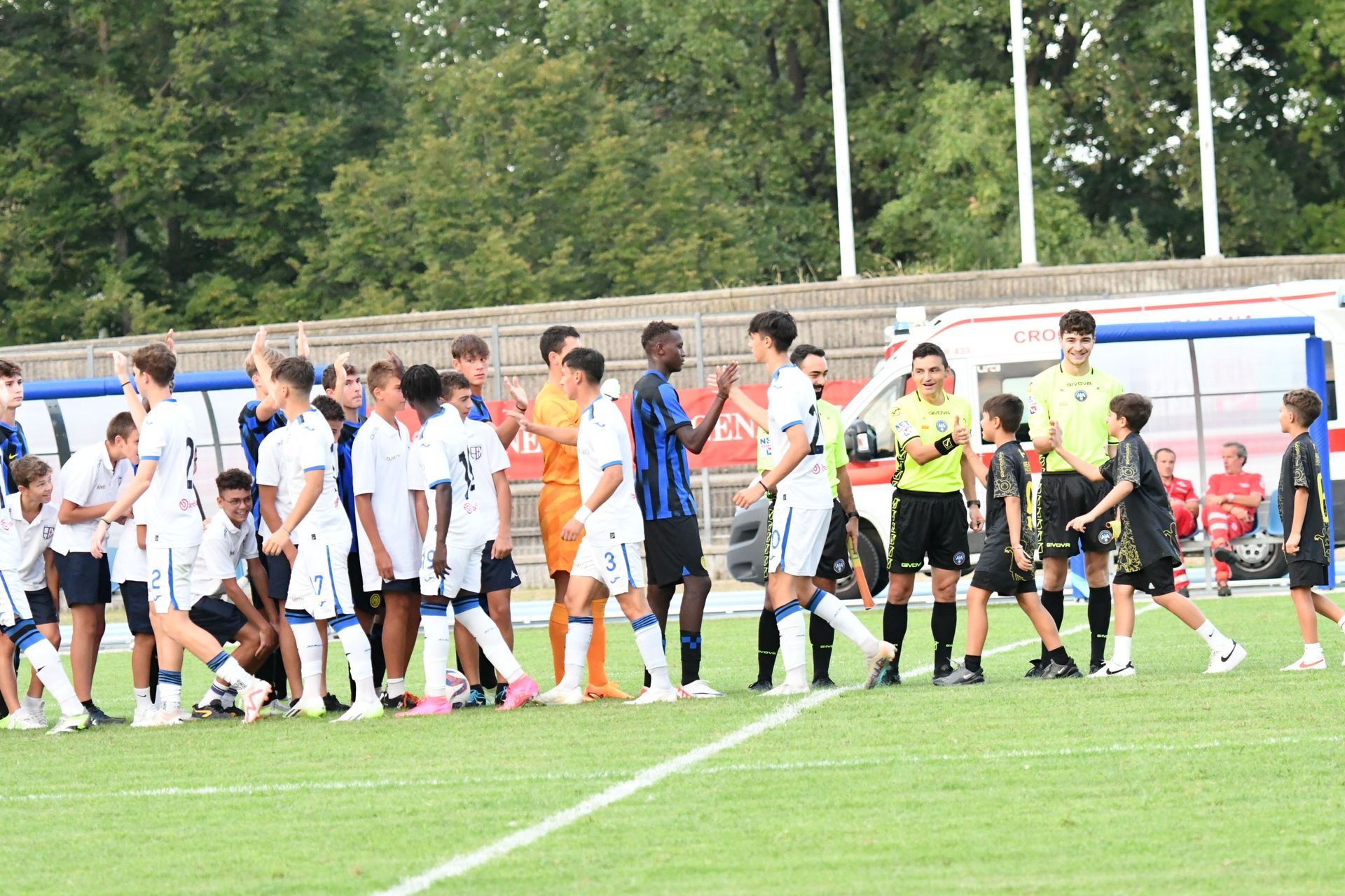 Giocatori di calcio in divisa blu e nera si stringono la mano su un campo verde. L'arbitro è in piedi nelle vicinanze.