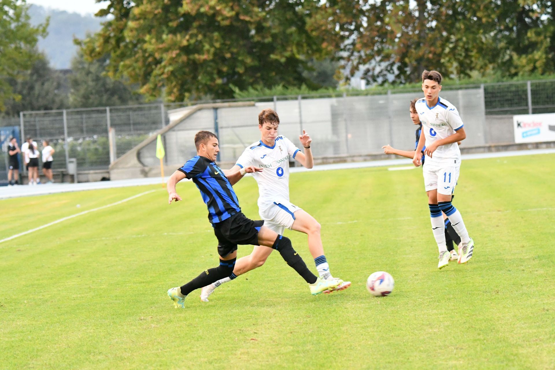 Giocatori di calcio in divisa blu e nera su un campo verde; uno di loro scivola per conquistare la palla.