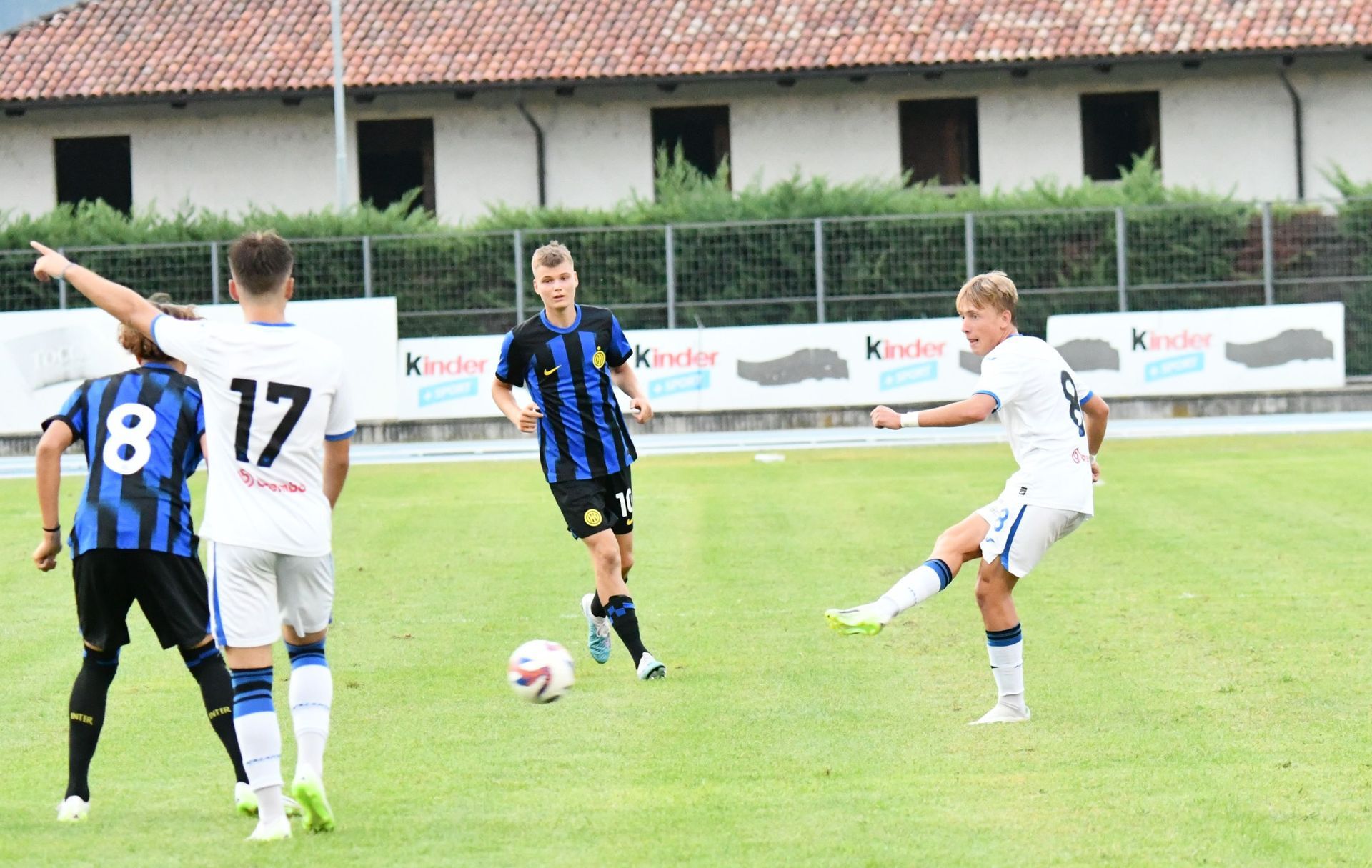 Un calciatore calcia un pallone durante una partita; gli altri giocatori in uniforme guardano.