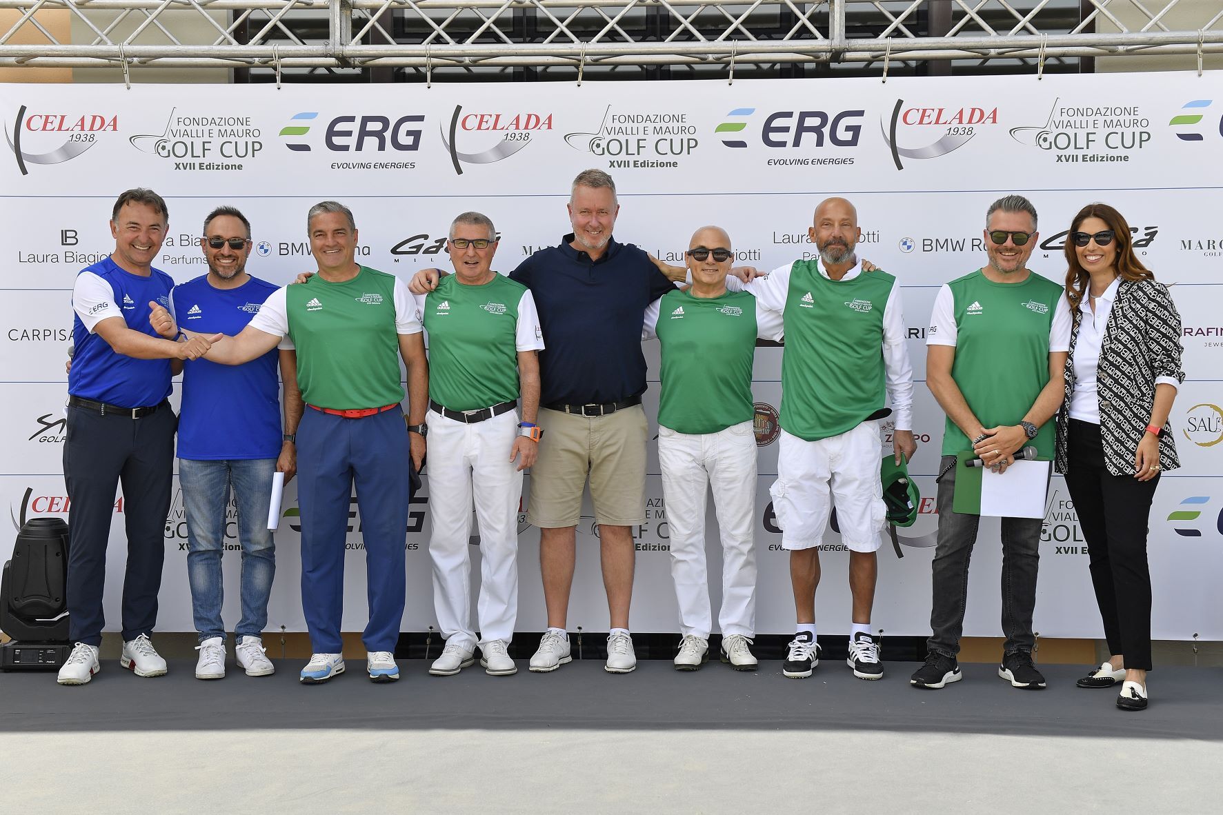 Un gruppo di persone in piedi su un palco, alcune delle quali indossano magliette verdi, sorridono e posano per una foto.