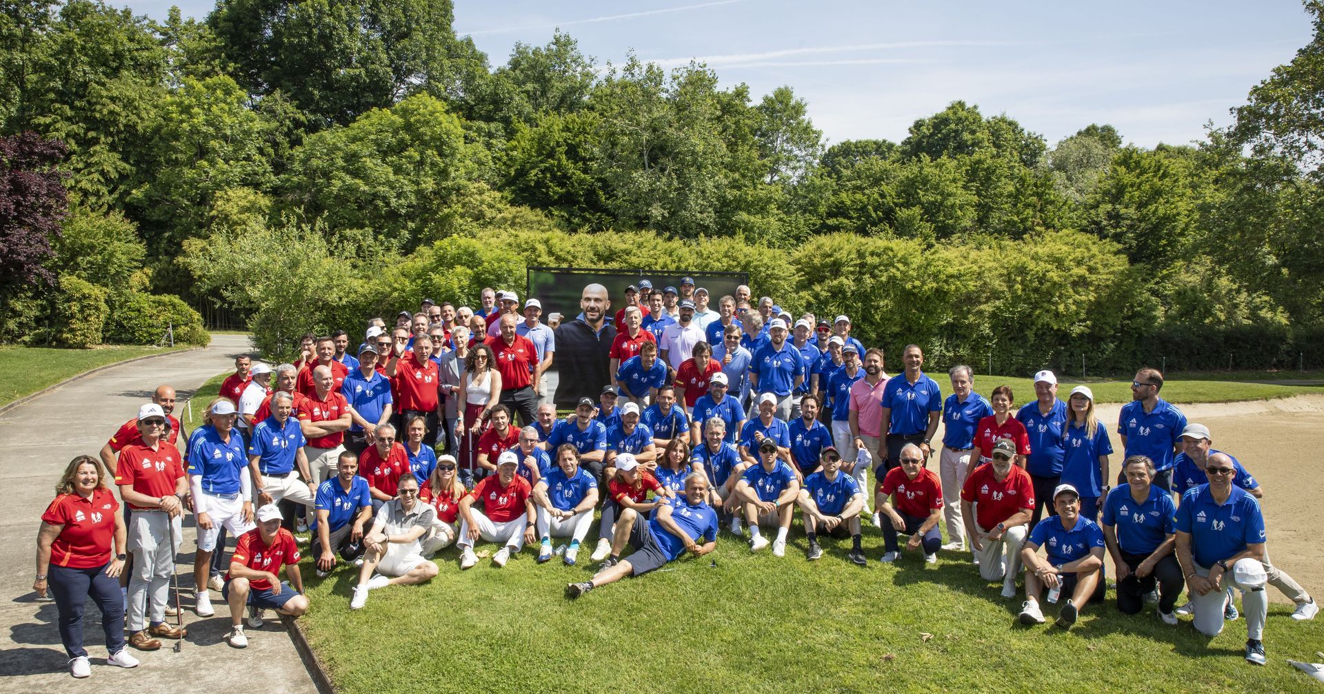 Gruppo di persone con magliette rosse e blu in posa sull'erba davanti agli alberi.