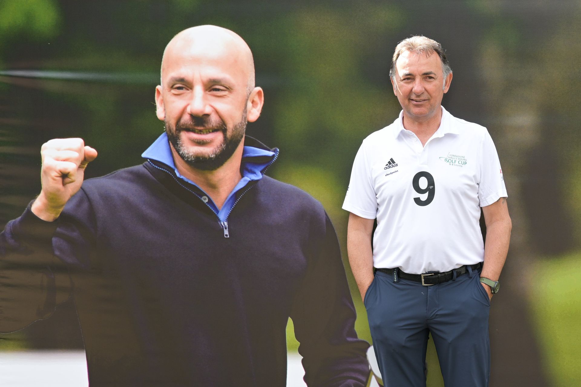 Un uomo con un maglione blu navy e un uomo con un abbigliamento da golf stanno in piedi davanti a uno sfondo sfocato.