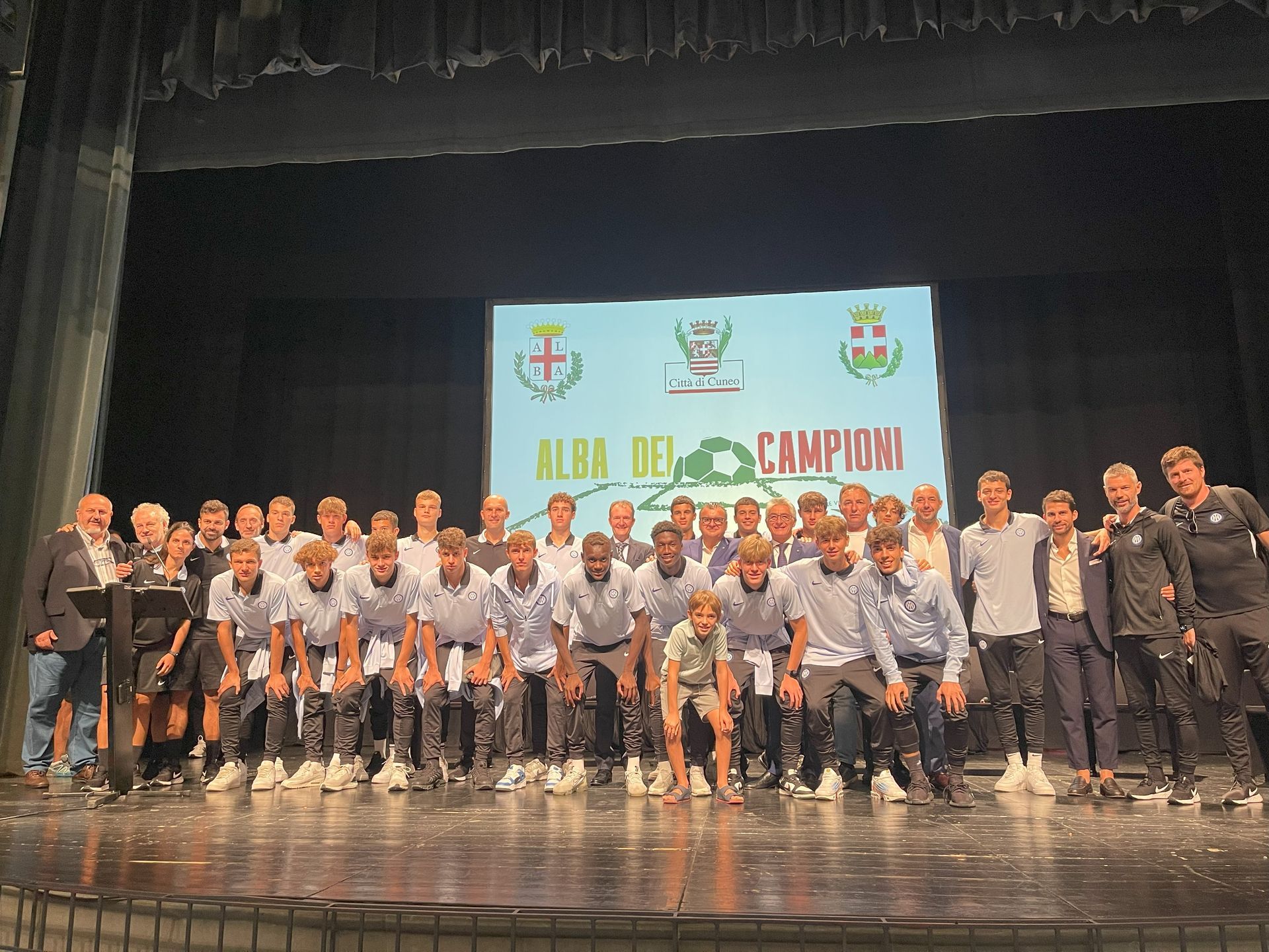 Una squadra con magliette abbinate su un palco celebra il campionato. Dietro di loro c'è uno striscione con i loghi.