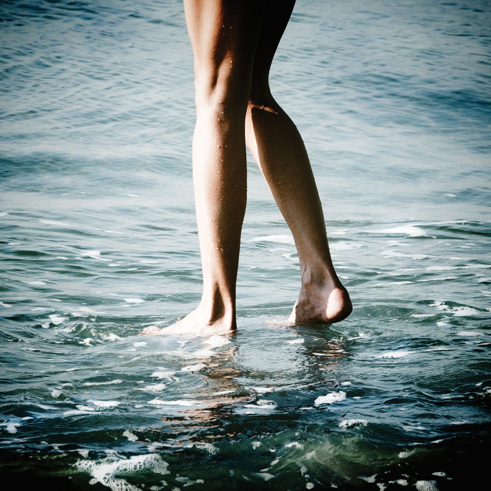 Gambe nude che camminano nell'acqua bassa dell'oceano.