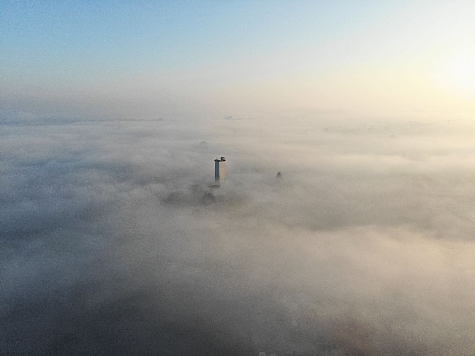 Torre che si erge sopra uno strato di nebbia, con un cielo limpido sullo sfondo.