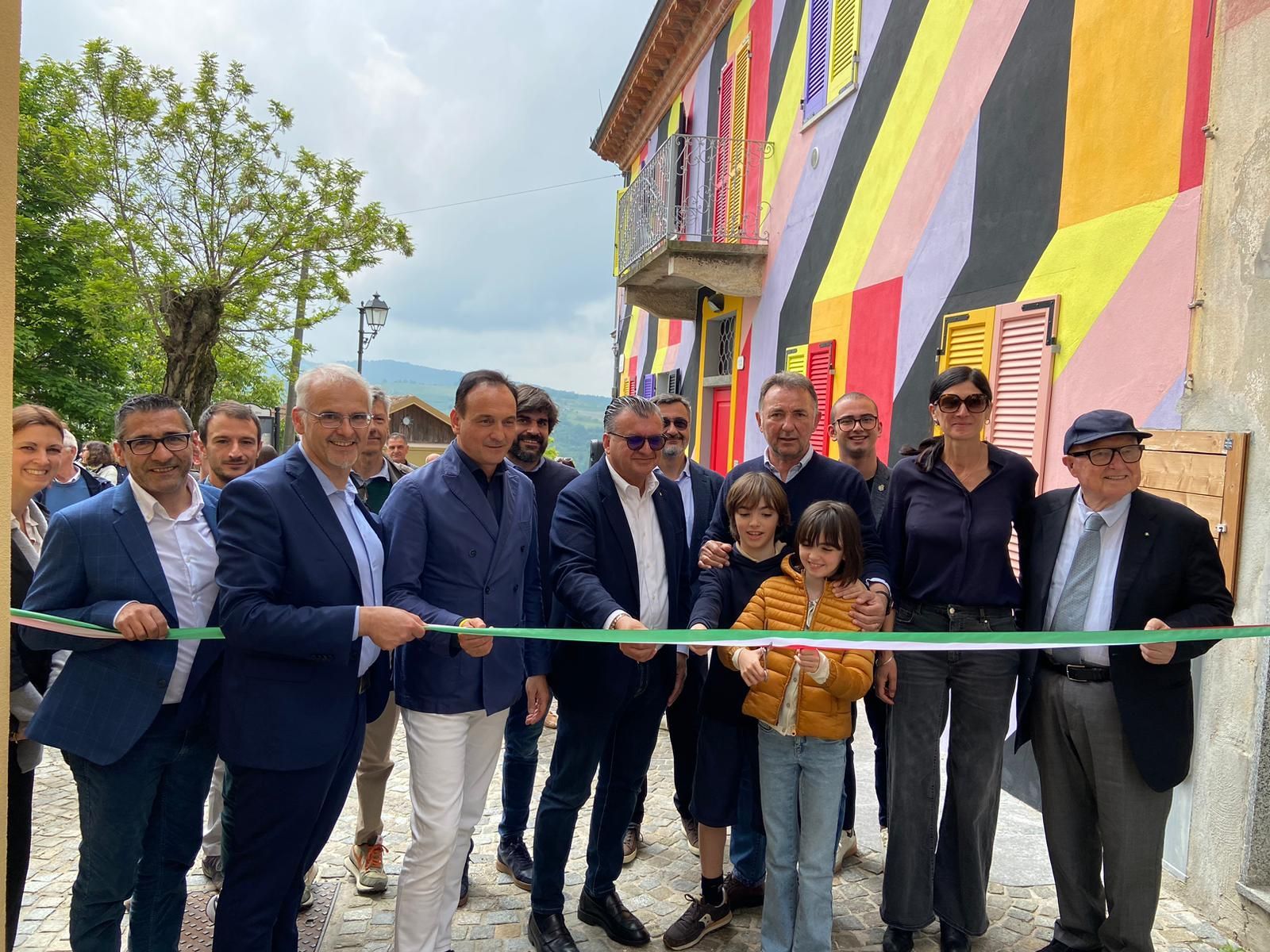 Persone che tagliano un nastro verde davanti a un murale colorato su un edificio.