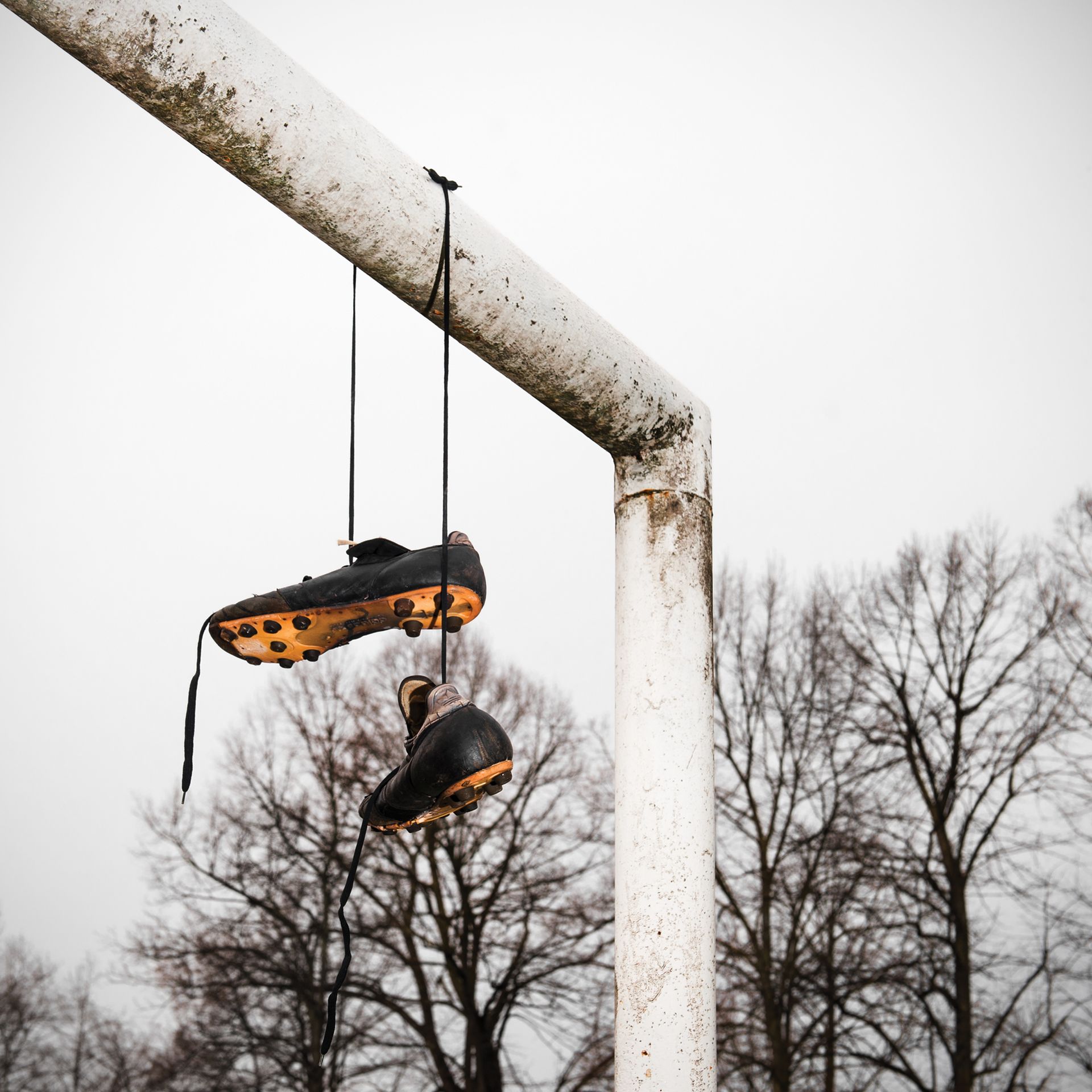 Scarpe da calcio appese a un palo della porta usurato contro un cielo nuvoloso.