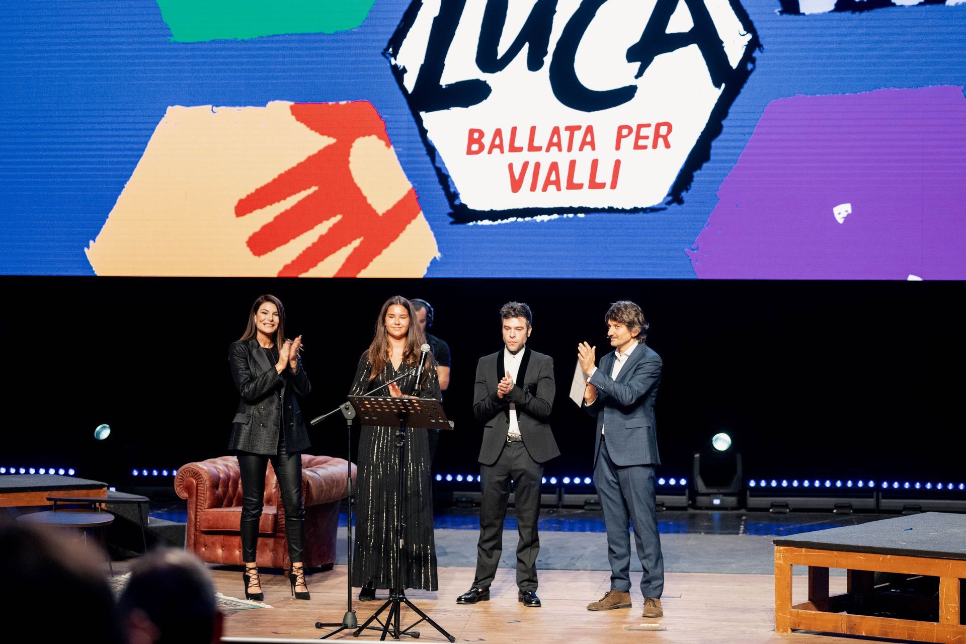 Persone che applaudono su un palco con uno schermo che mostra 