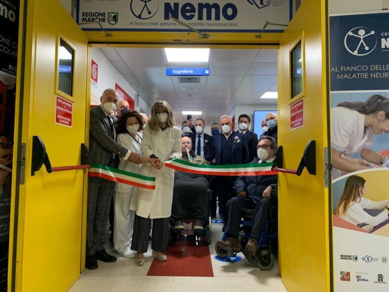 Persone che tagliano un nastro all'ingresso di una struttura medica. Il nastro è verde, bianco e rosso.