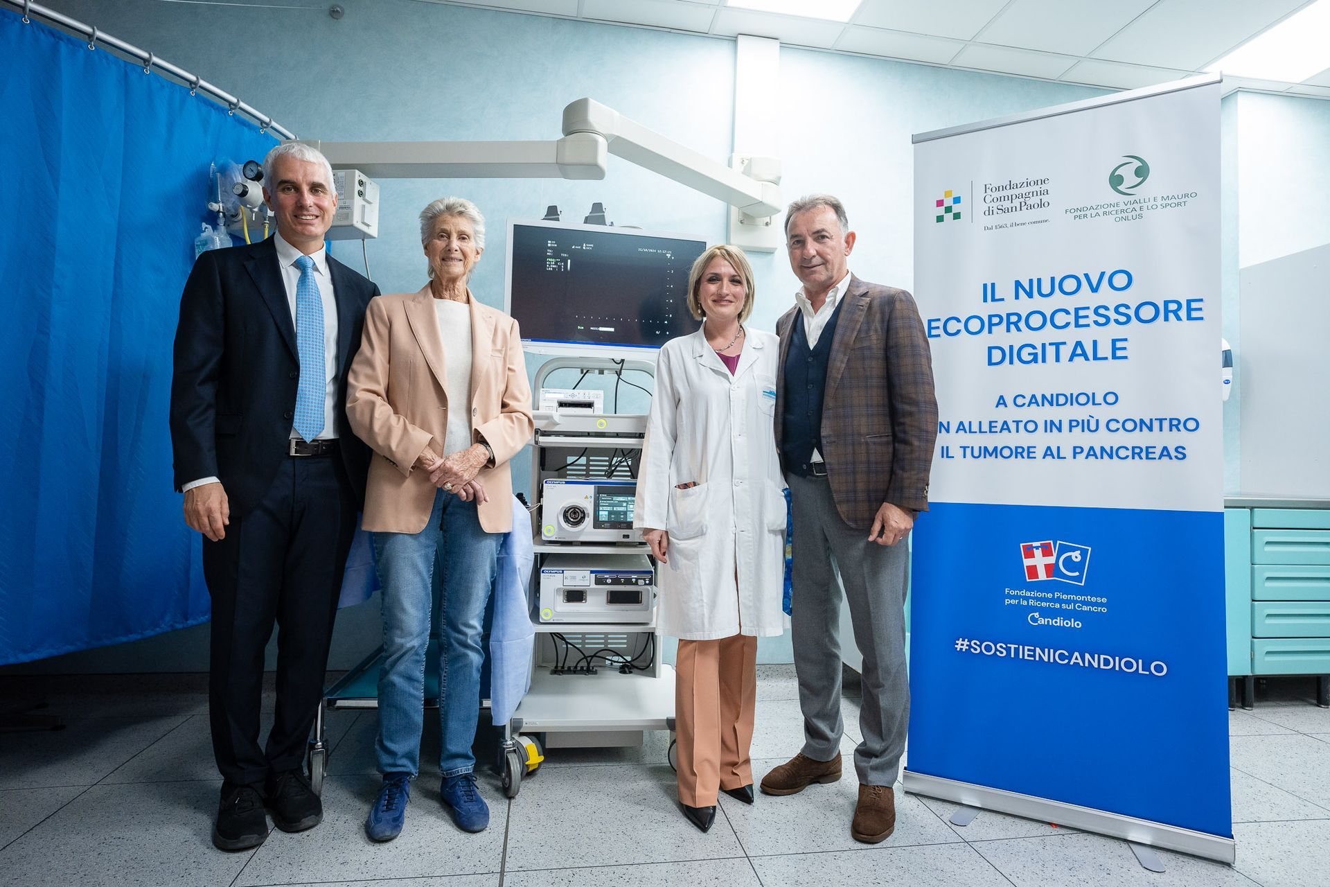 Quattro persone in piedi accanto ad apparecchiature mediche. Uno striscione recita 