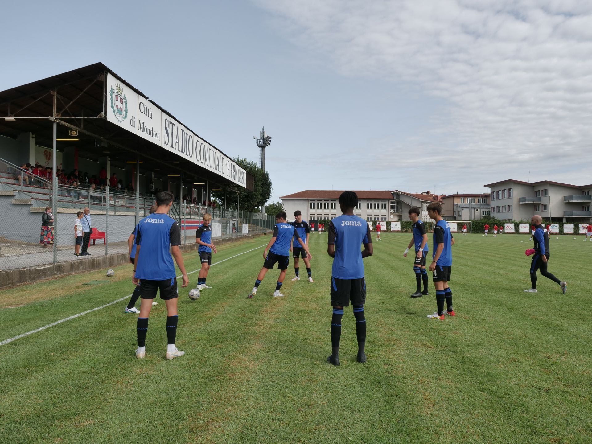 Giocatori di calcio in divisa blu e nera si stendono su un campo verde di fronte a uno stadio.
