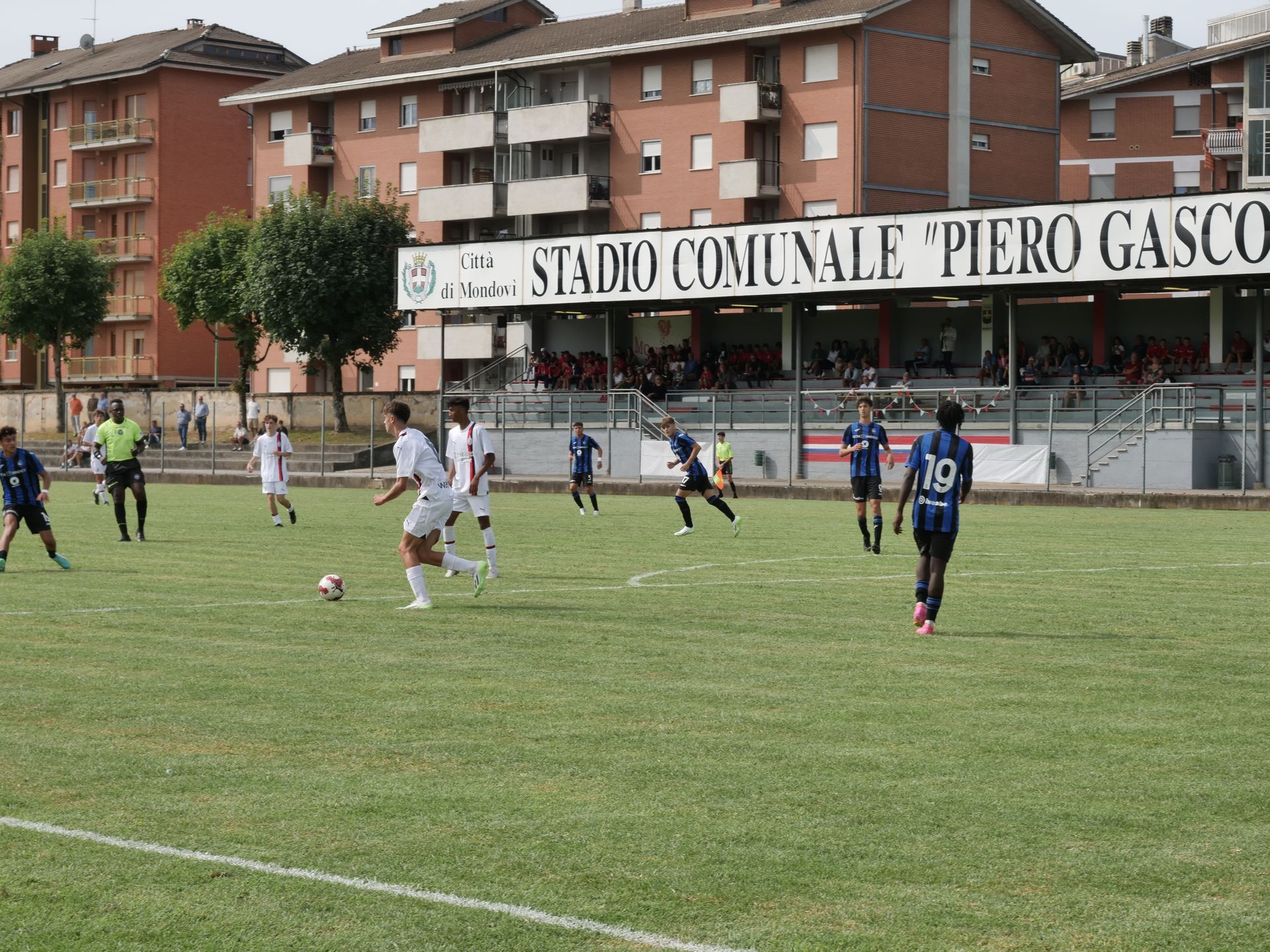 Partita di calcio allo Stadio Comunale Piero Gasco. Giocatori in azione sul campo verde, spettatori sugli spalti.