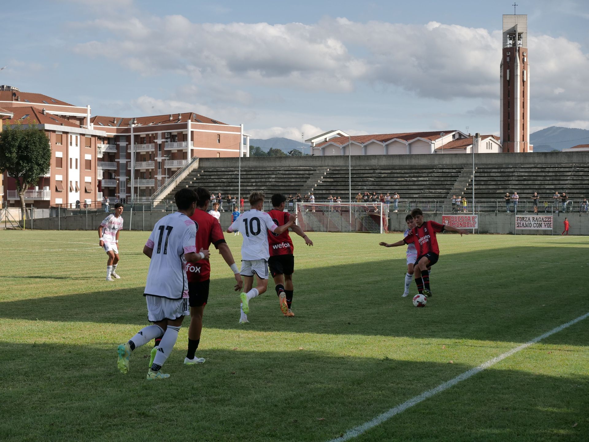 Giocatori di calcio in divisa bianca e rossa su un campo verde. Sono visibili uno stadio e un'alta torre.