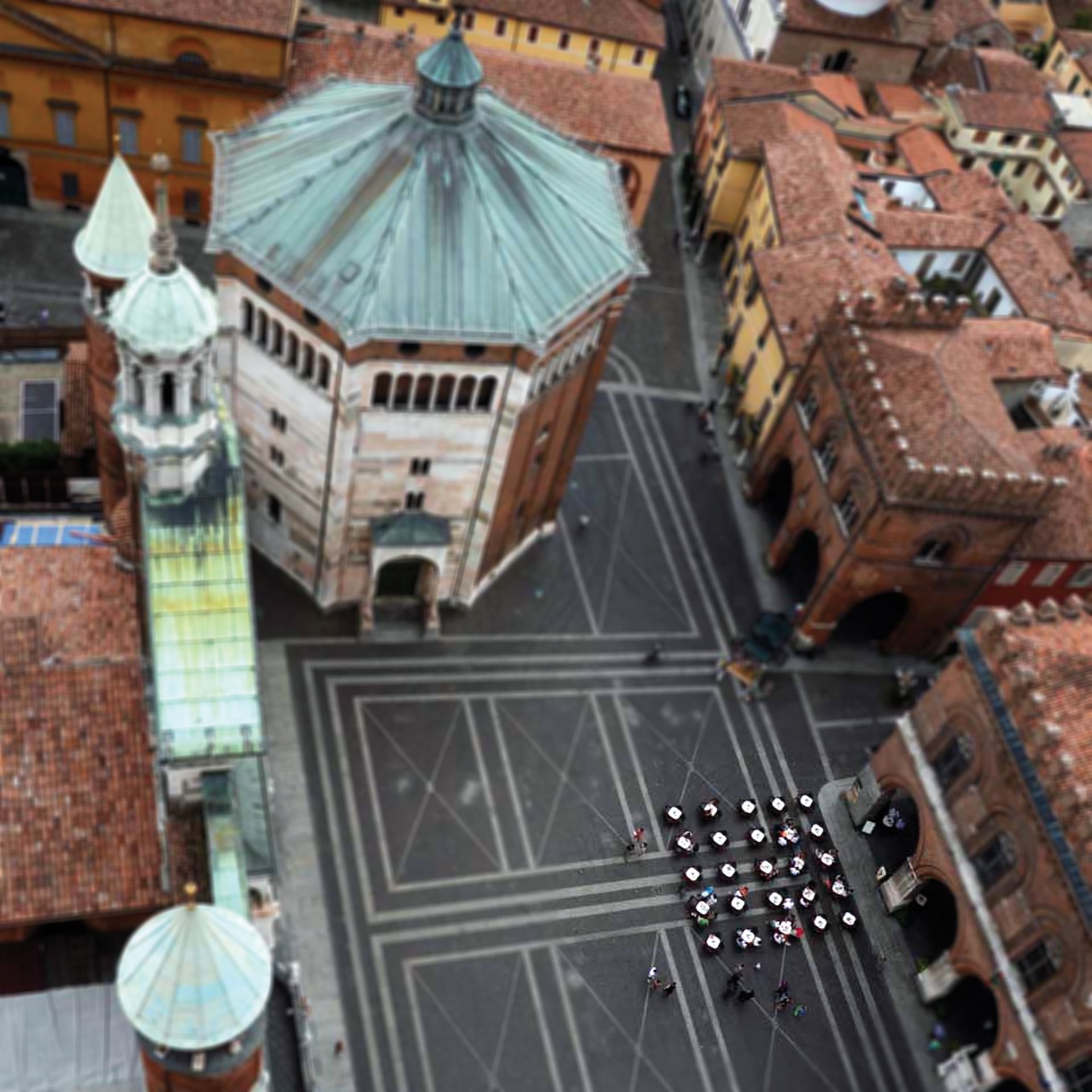 Vista aerea di una piazza di Cremona, in Italia, con uno storico battistero ottagonale ed edifici con tetti di tegole rosse.