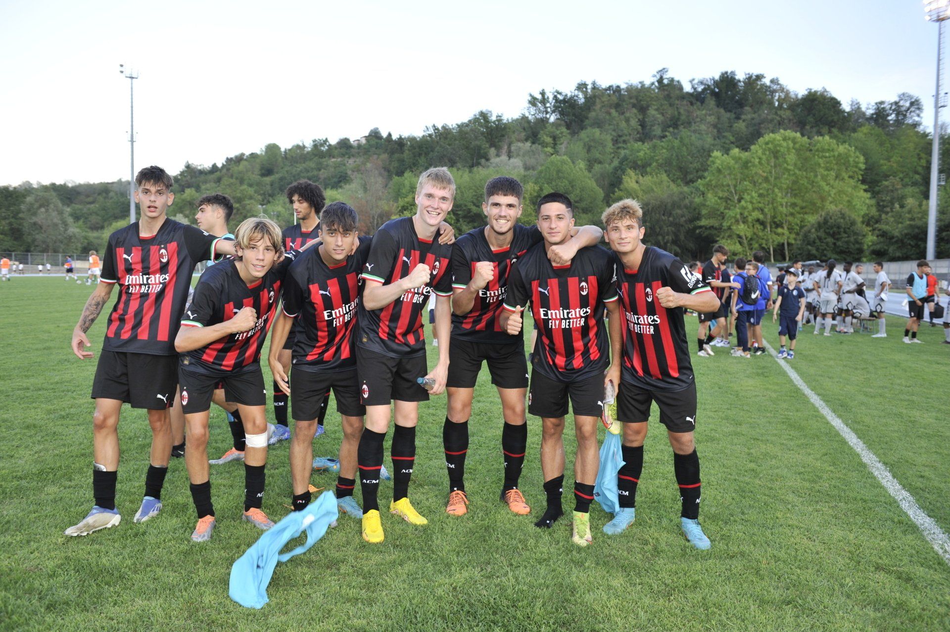 La squadra di calcio in divisa nera e rossa festeggia su un campo verde. Sullo sfondo, alberi e una collina.