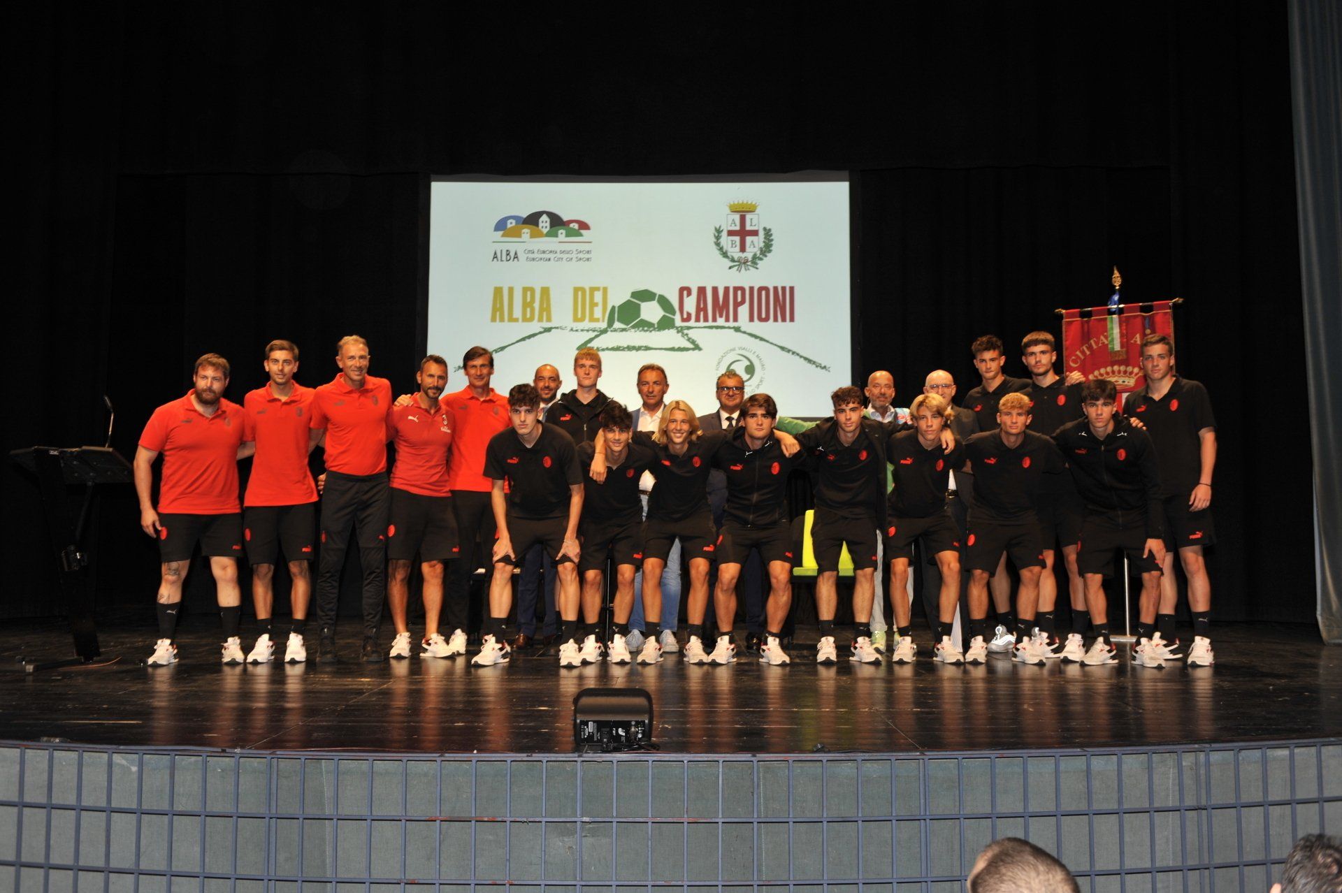 Un gruppo di persone in uniforme rossa e nera su un palco, in posa per una foto.