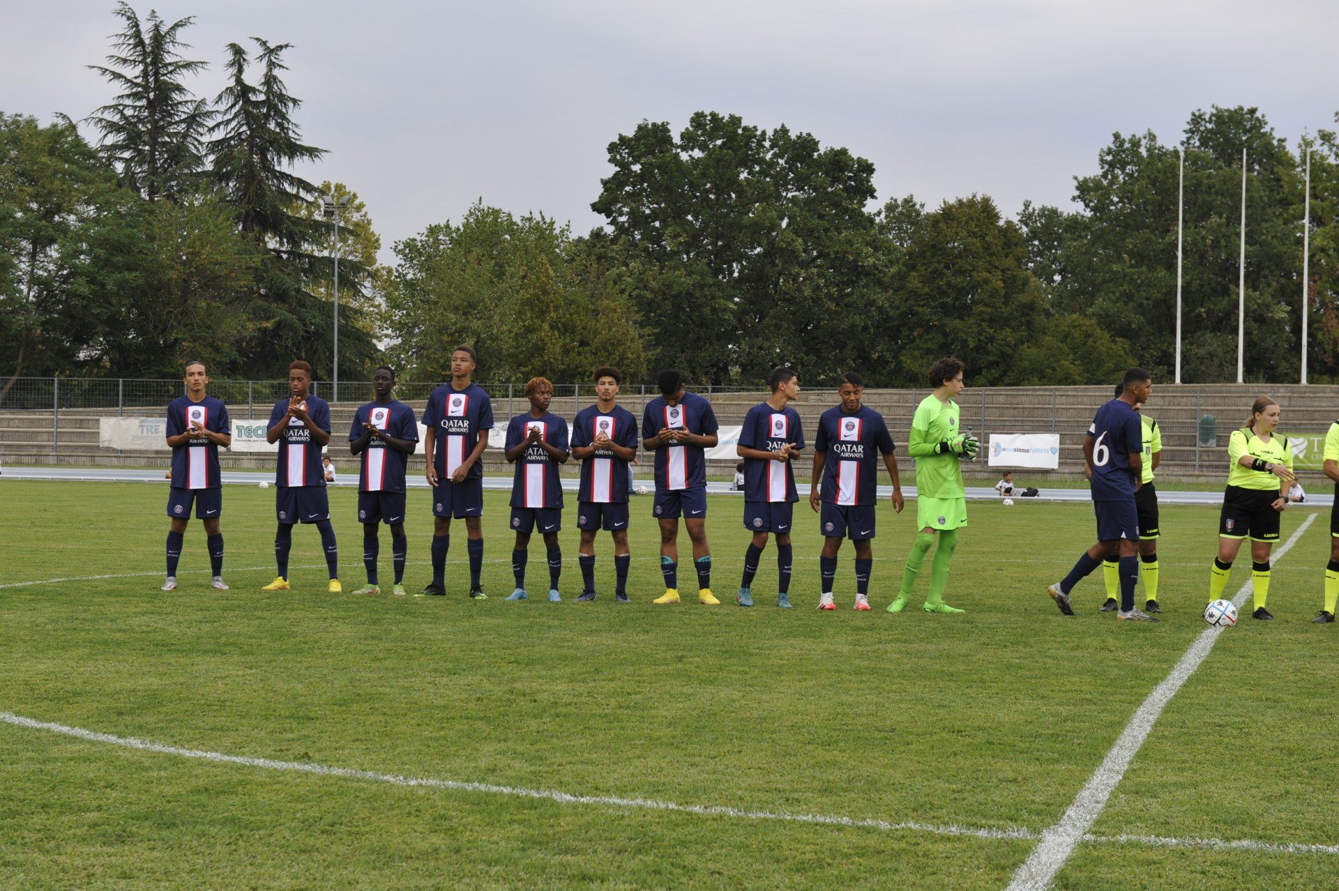 I giocatori di calcio con le maglie blu e bianche si allineano su un campo verde. Un arbitro è in piedi nelle vicinanze.