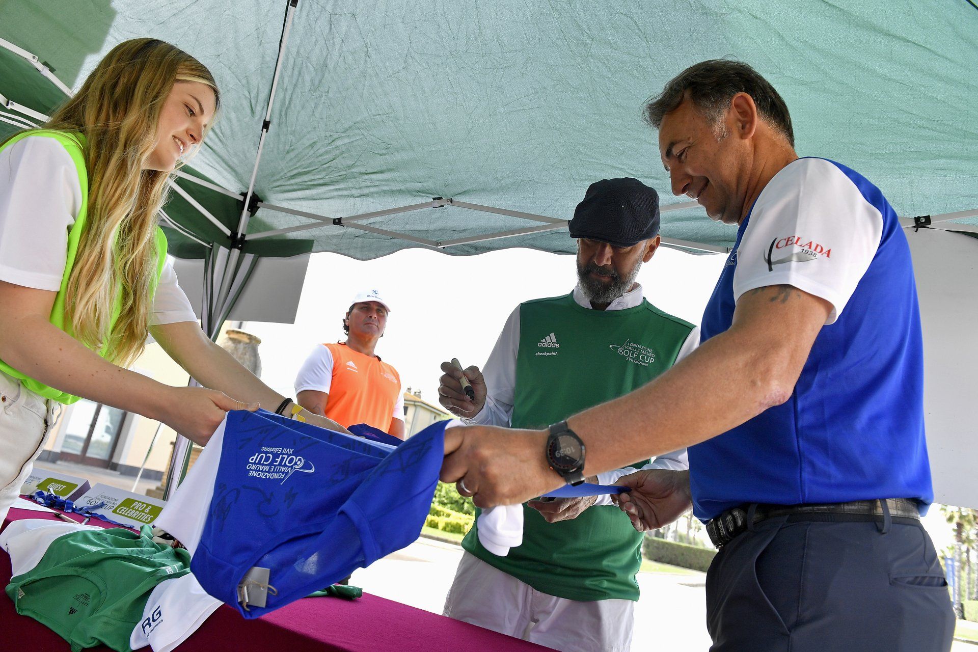 Persone che partecipano a un evento di golf mentre si registrano. Una donna e due uomini sono seduti a un tavolo sotto una tenda.