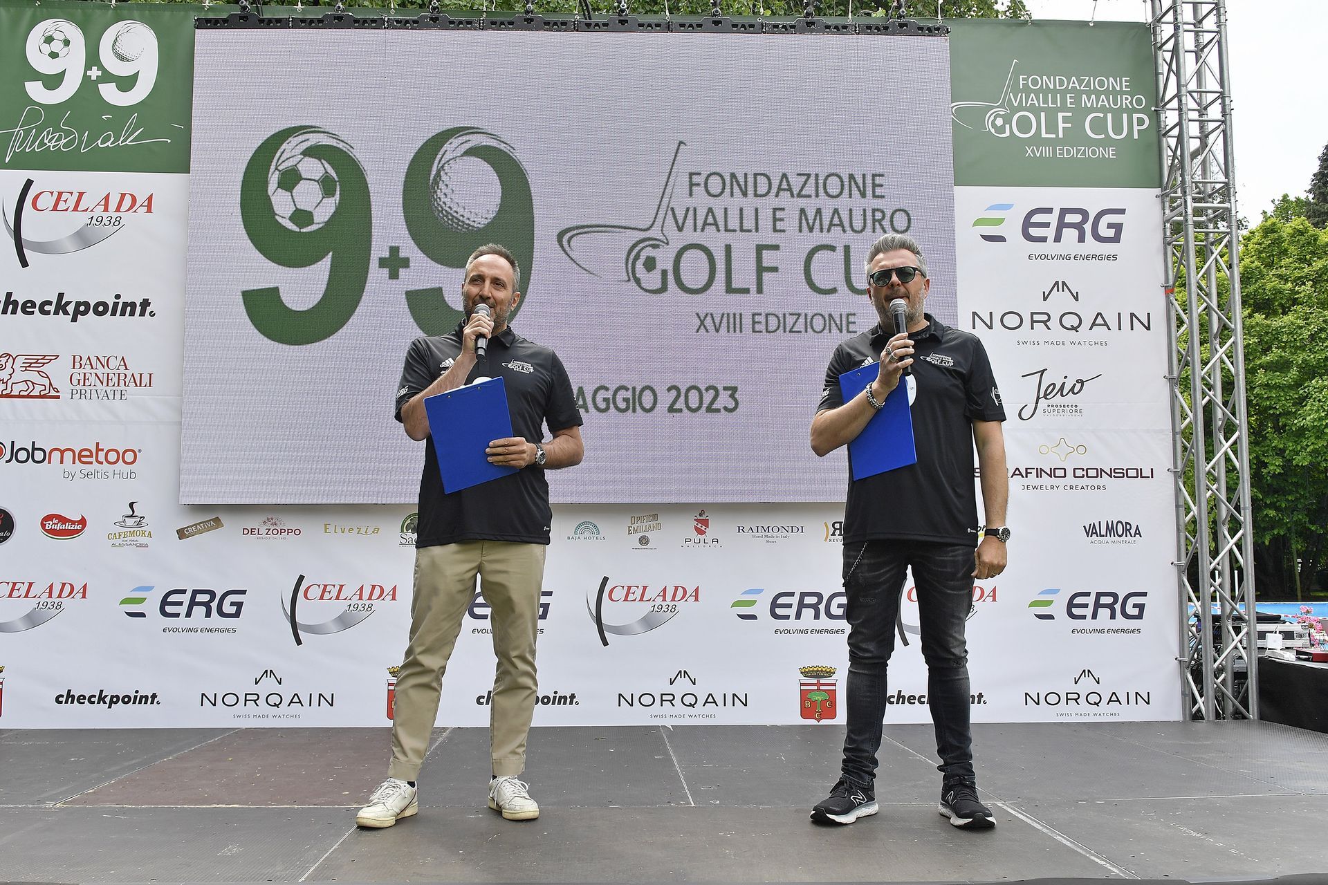 Due uomini su un palco con microfoni, uno sfondo con loghi e testi per un evento di golf cup in Italia.