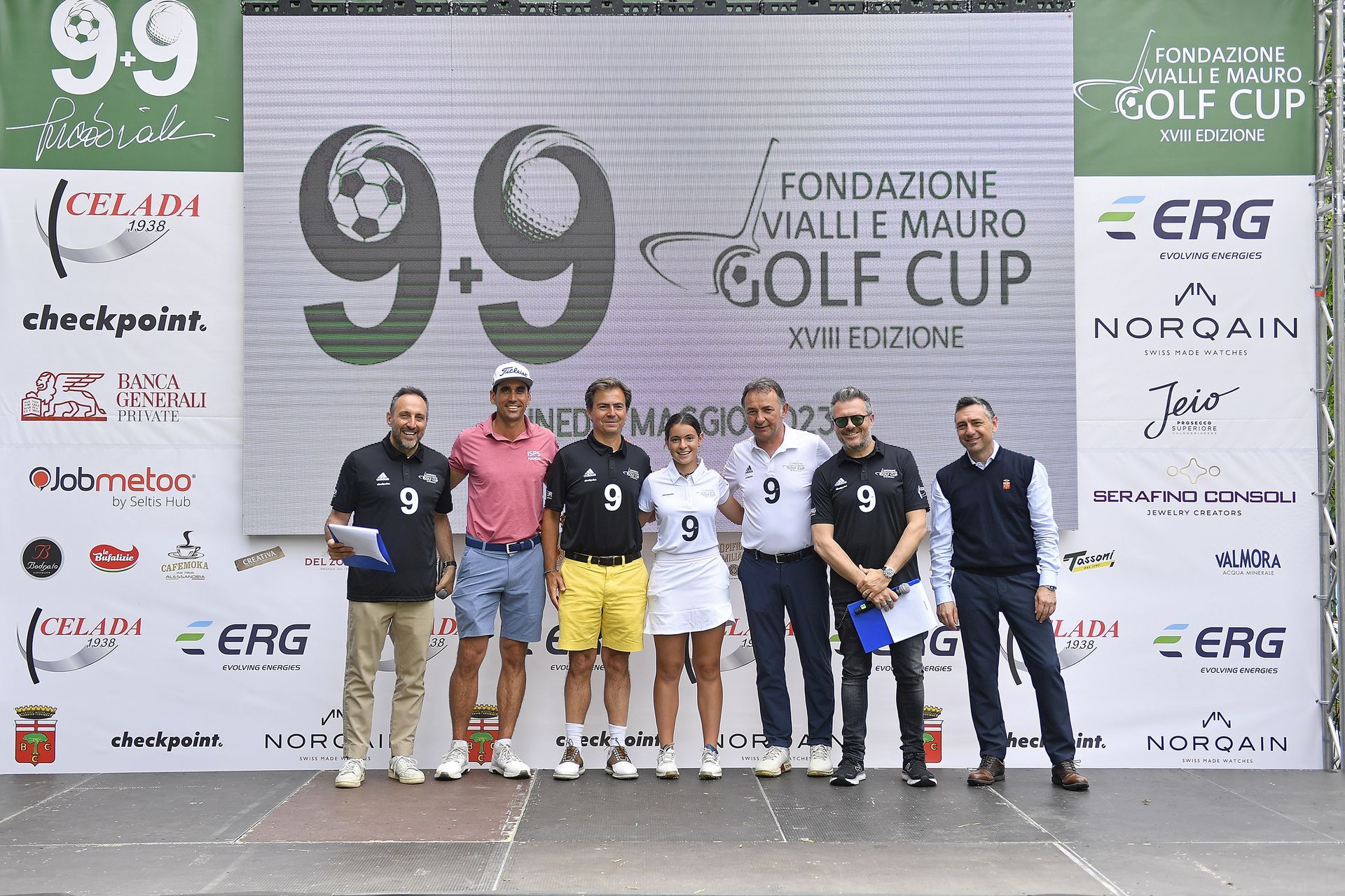 Gruppo di persone in posa su un palco durante una gara di golf. Un grande schermo mostra il nome dell'evento e gli sponsor.