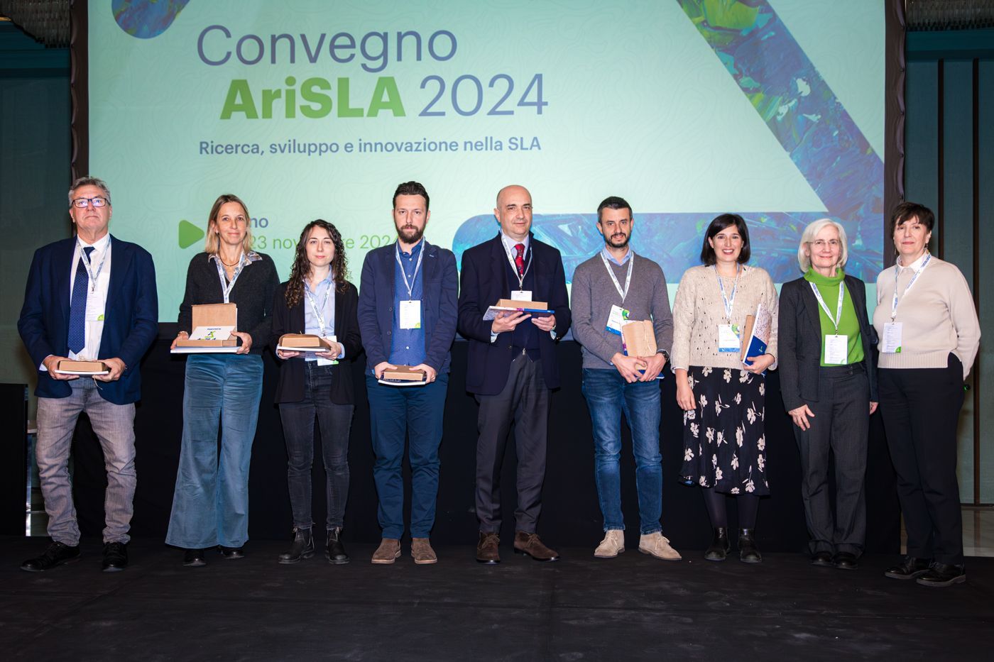 Gruppo di persone che tengono i premi su un palco con uno striscione della conferenza, 