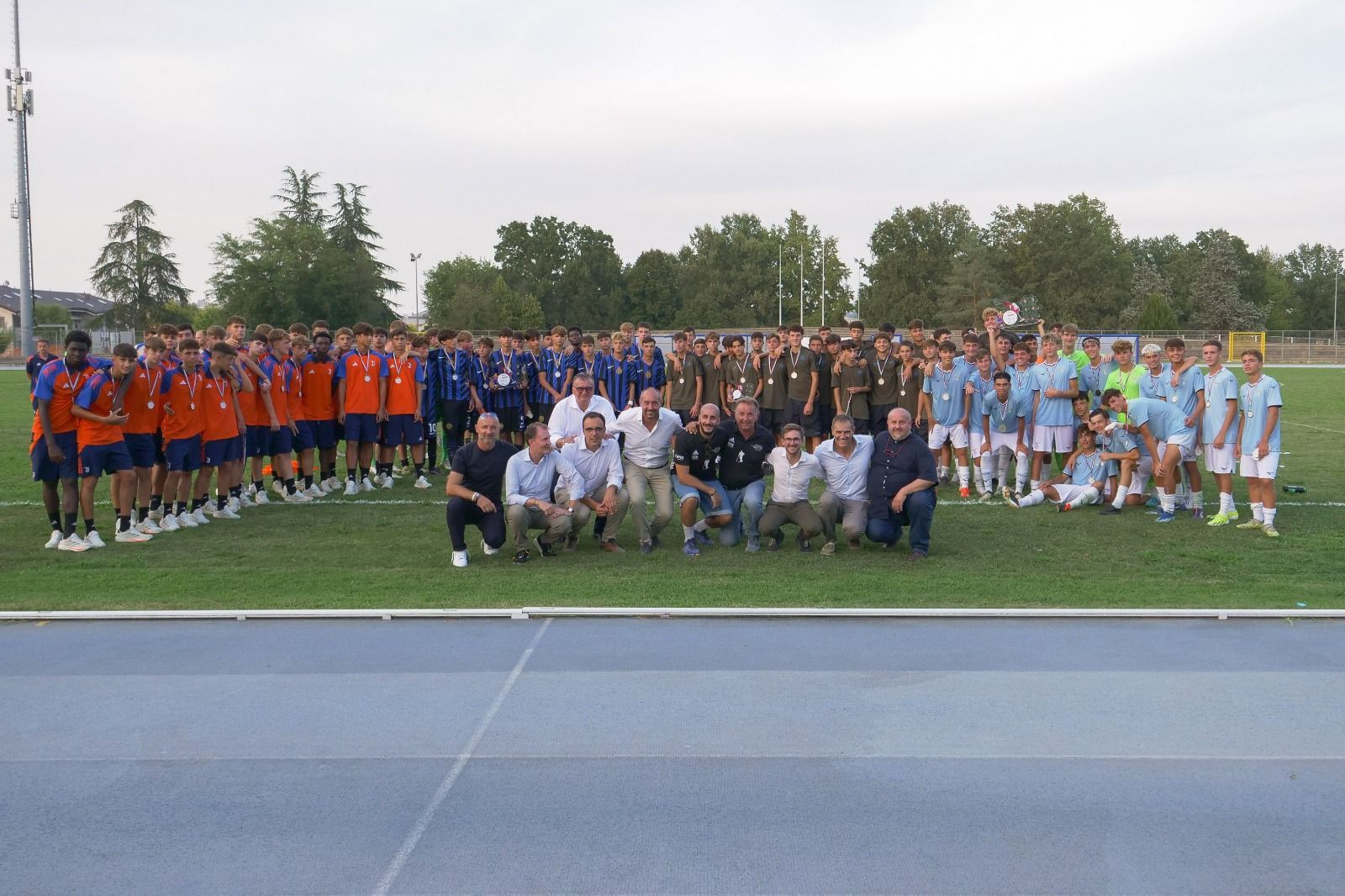 Squadre di calcio in divise arancioni e azzurre e altre persone sono in piedi su un campo.
