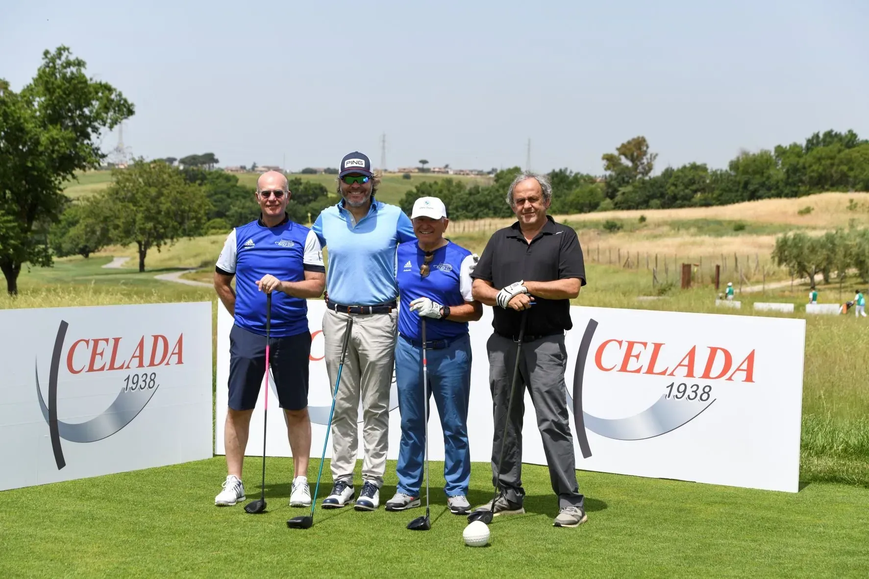 Quattro uomini su un campo da golf posano vicino alla segnaletica Celada 1918, tenendo in mano le mazze; giornata di sole.