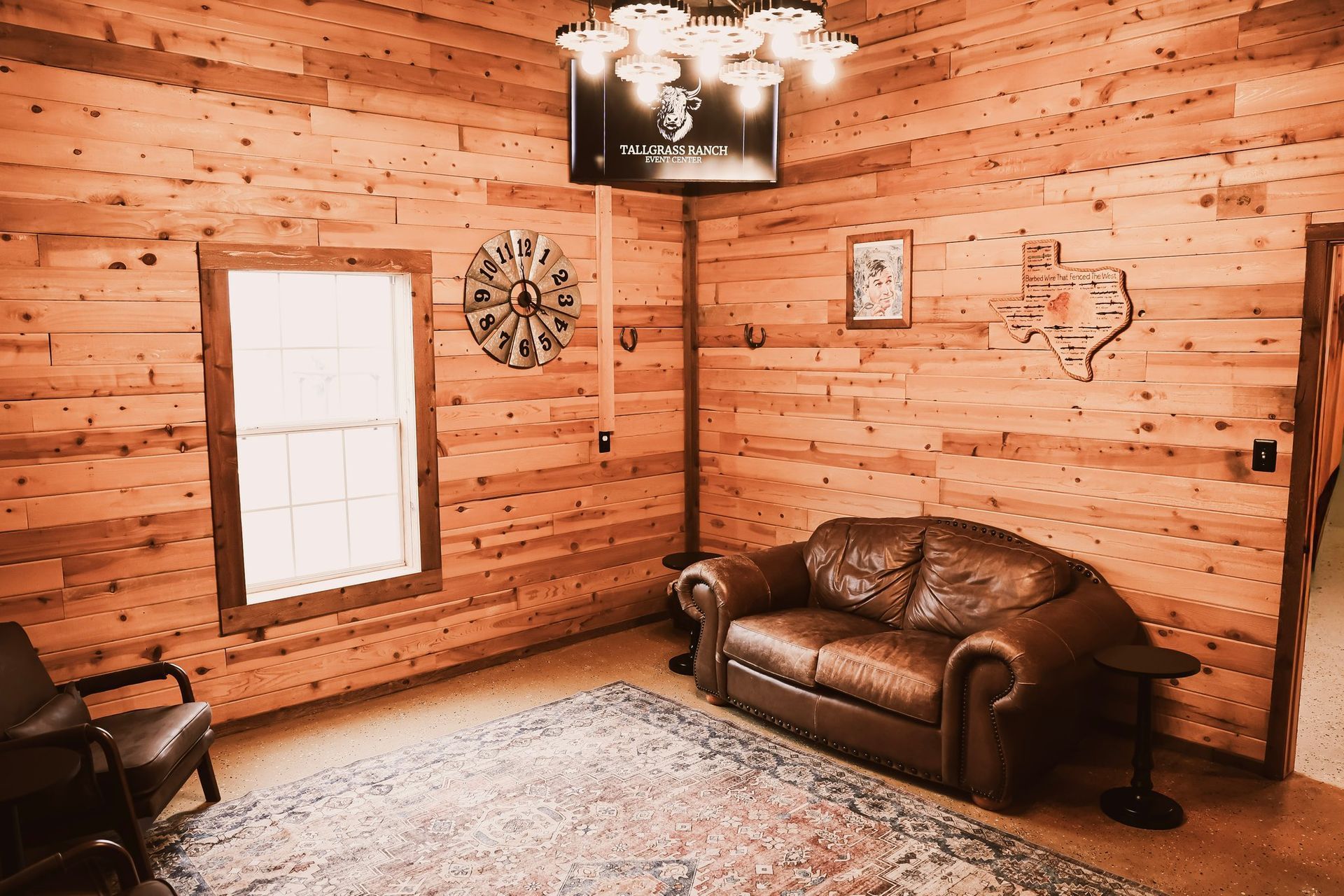 Wooden-walled room with leather sofa, rug, and window. Decorative clock, art, and lighting fixtures are visible.