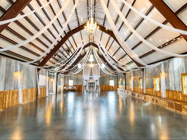 Spacious, well-lit wedding venue with draping, chandeliers, and polished concrete floor.