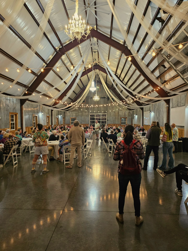 Large event space with tables, guests, and decorative lighting. A person stands facing away from the camera.