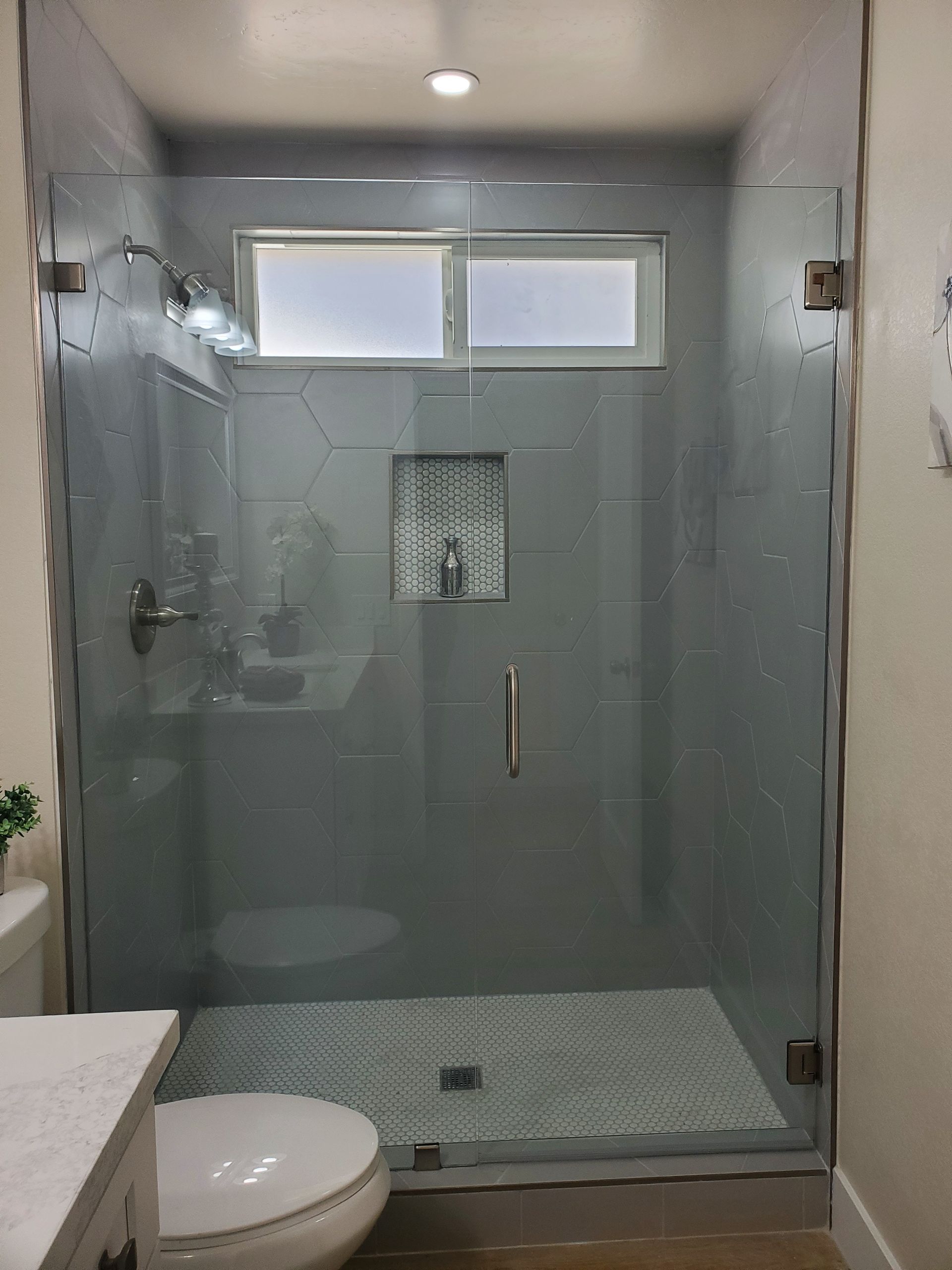 Modern glass-enclosed shower with gray tiled walls, a decorative inset niche, and patterned floor tile.