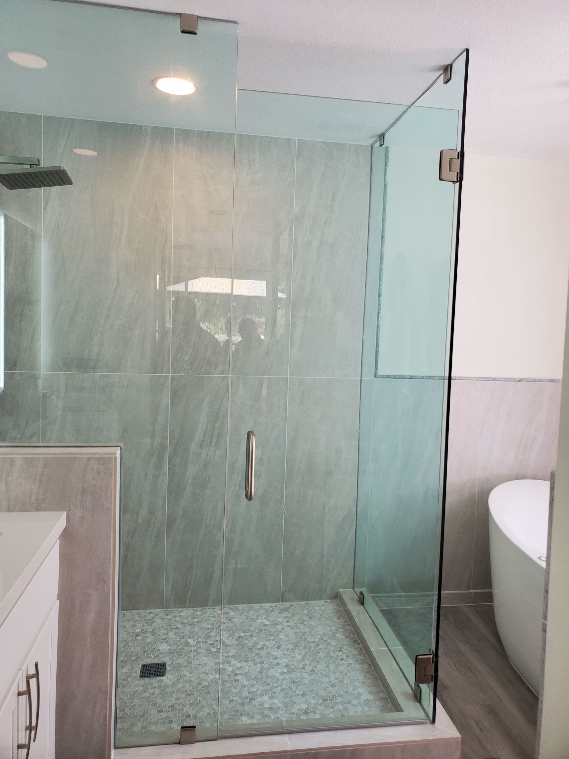A glass-enclosed shower with gray tiled walls and a light-colored pebbled floor in a modern bathroom.