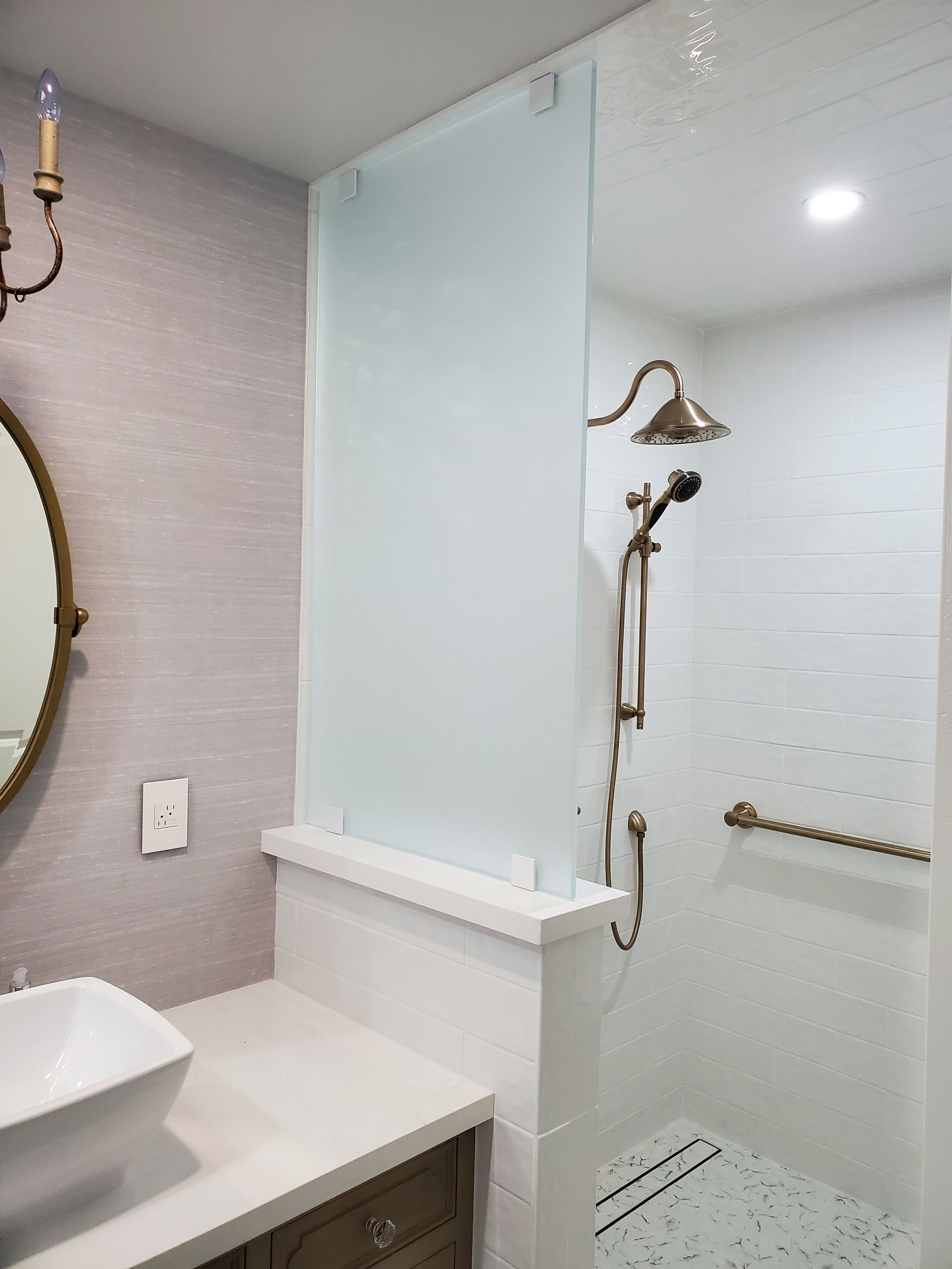 A bathroom featuring a white vanity with a vessel sink, a frosted glass shower partition, and a bronze shower fixture.