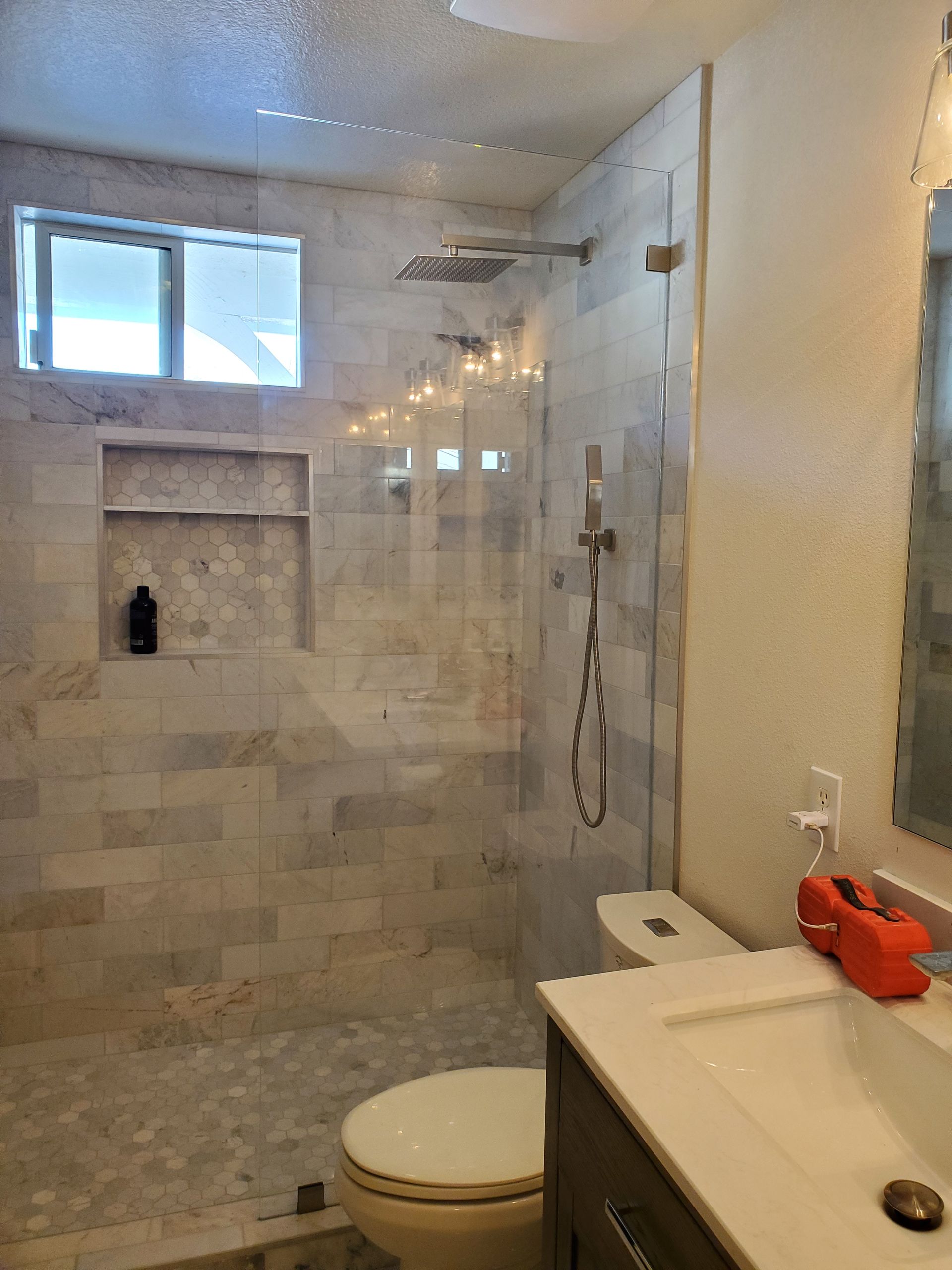 A modern bathroom with a glass-enclosed shower, stone-tiled walls, a built-in shower niche, and a vanity sink.