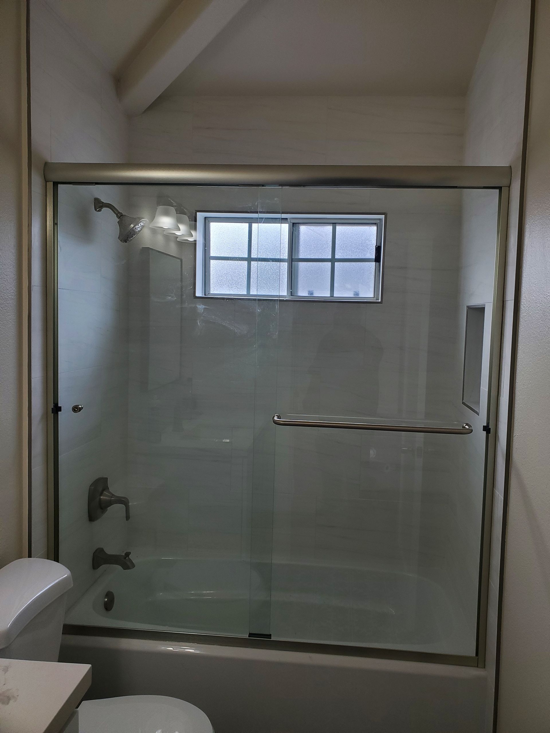A bathroom bathtub and shower unit with a sliding glass door and a small, rectangular window on the back wall.
