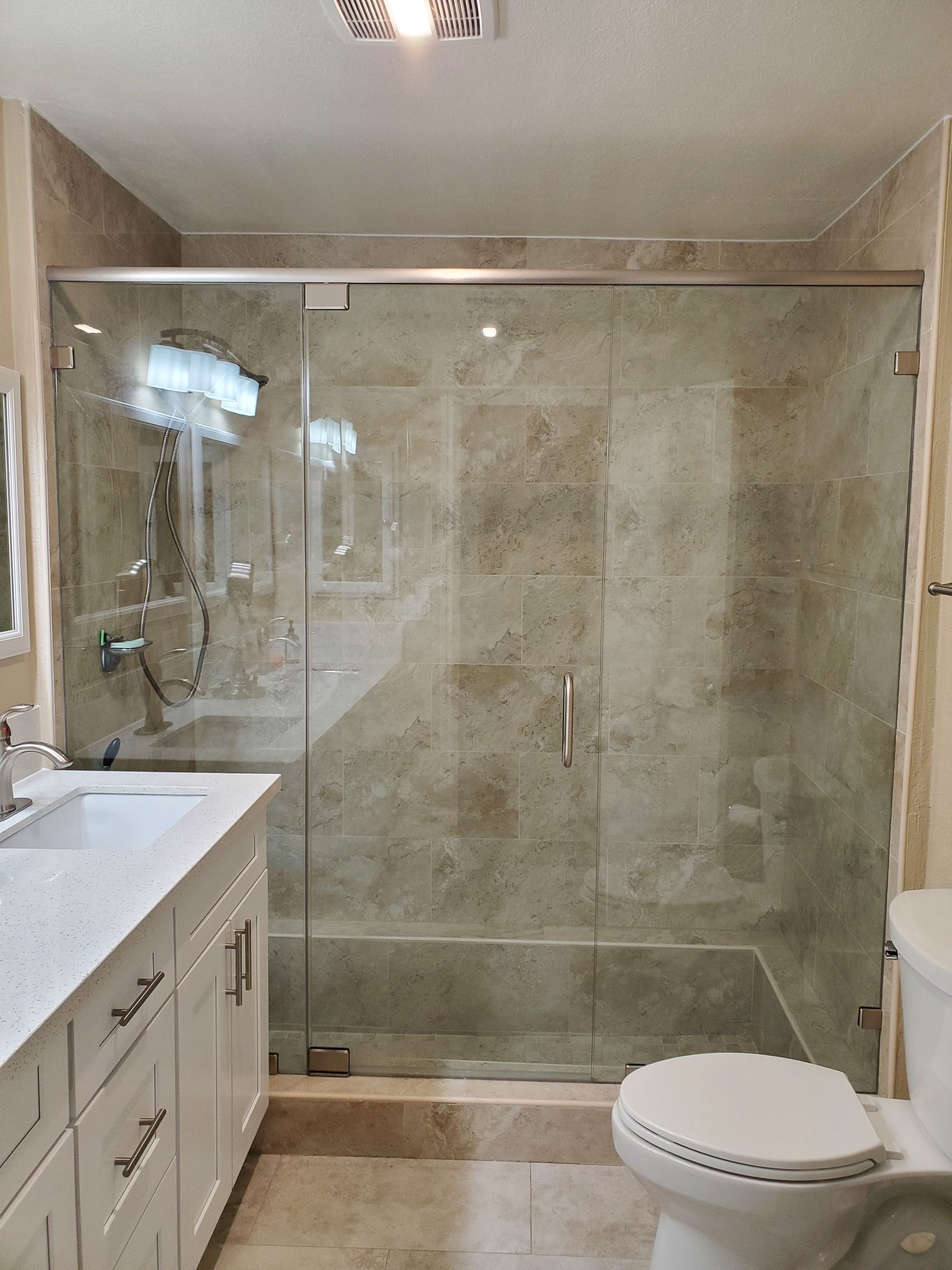 A bathroom with a tiled walk-in shower enclosed by a frameless glass door, next to a white vanity and toilet.