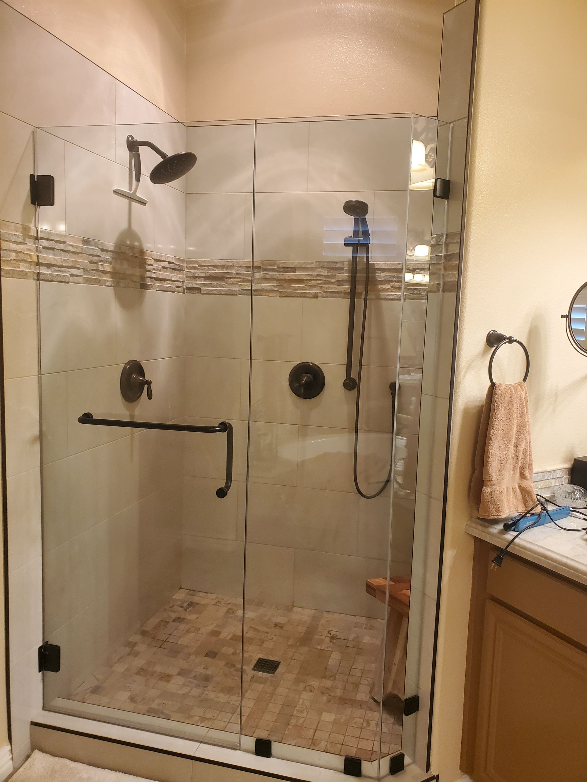 A glass-enclosed shower with tiled walls and flooring, featuring a dual-head shower system and dark fixtures.