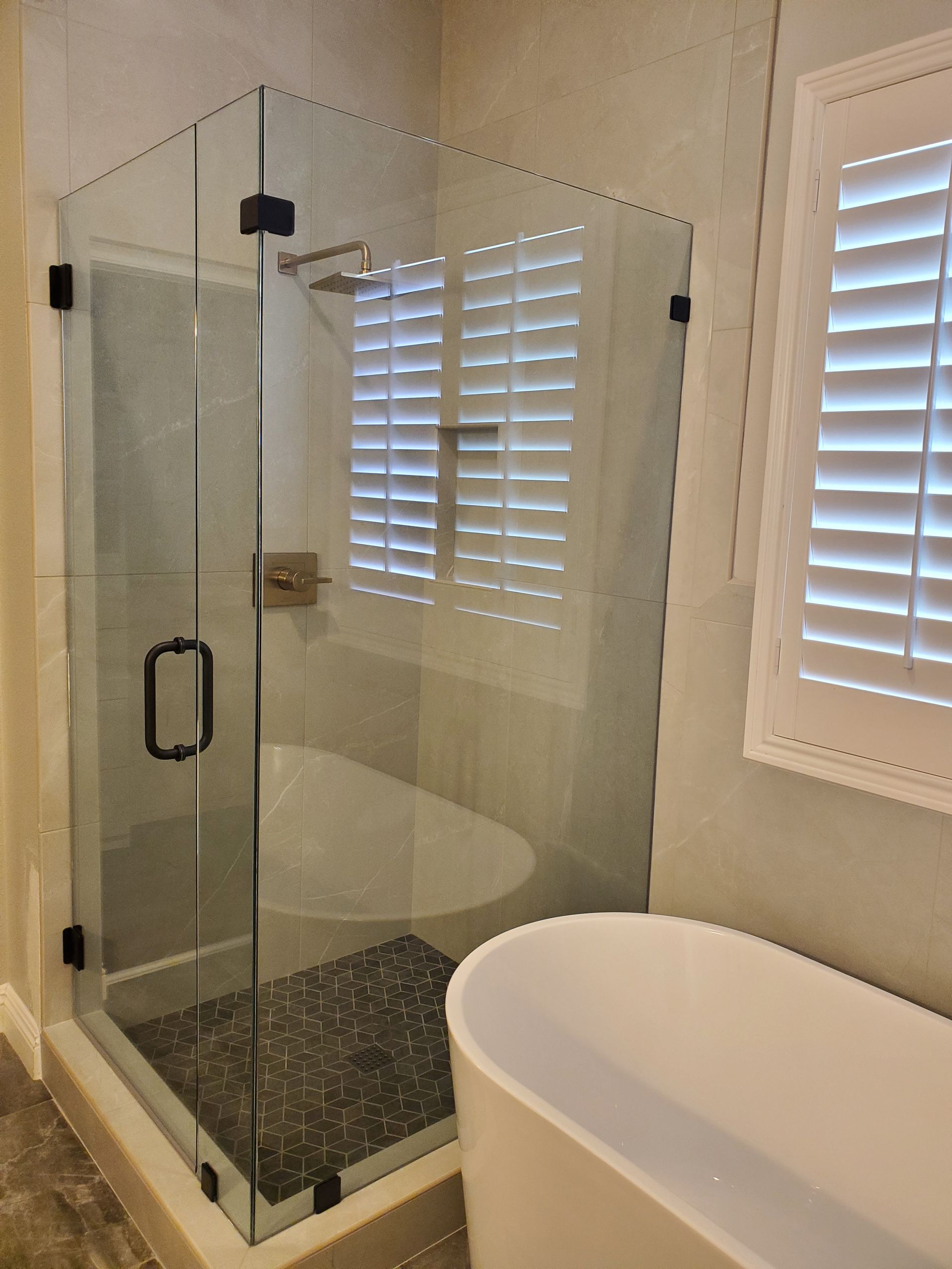 Modern bathroom featuring a corner glass walk-in shower with black hardware next to a freestanding white bathtub.