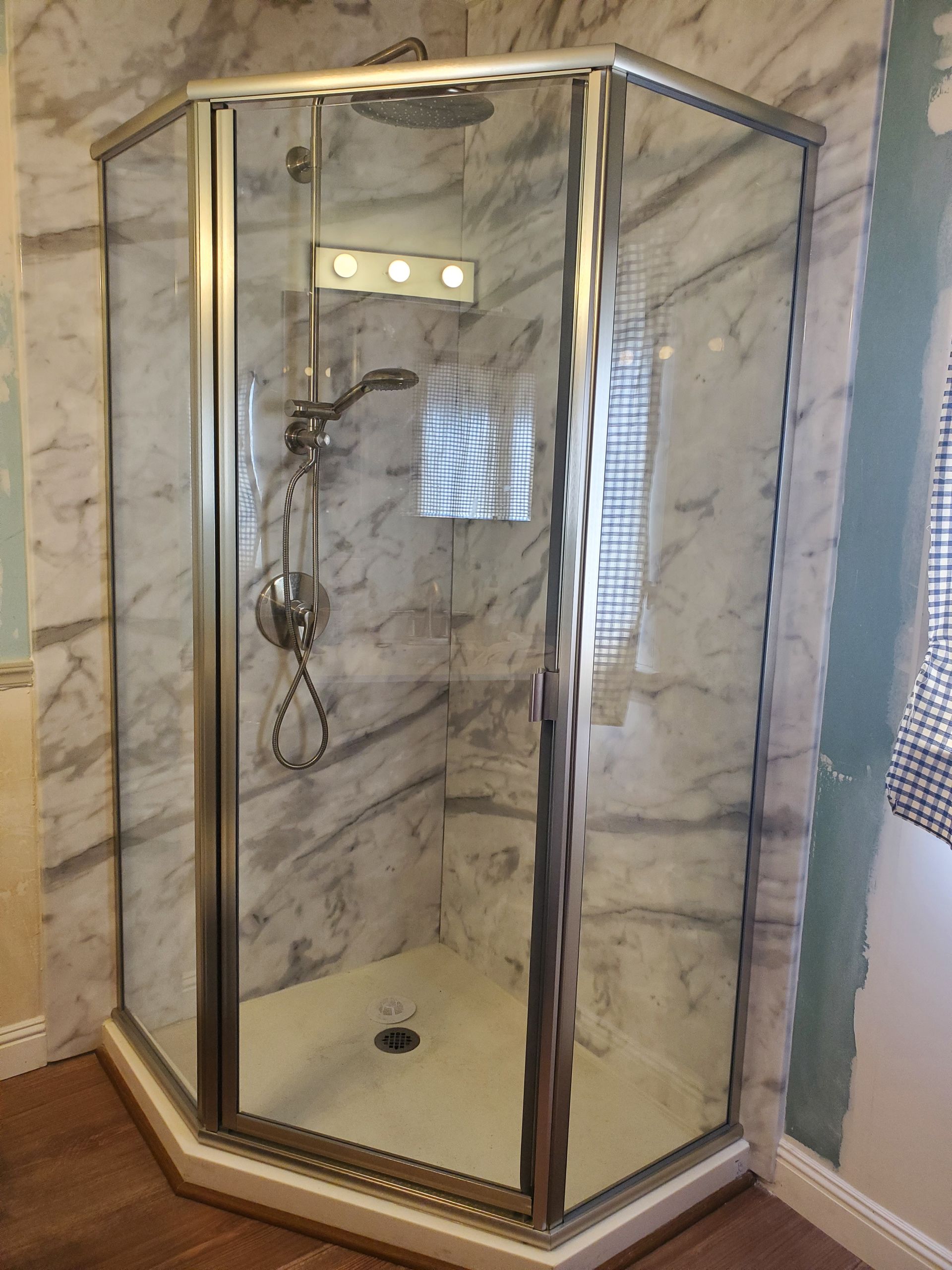 Corner shower enclosure with glass doors, silver frame, chrome shower fixture, and marble-patterned tile walls.