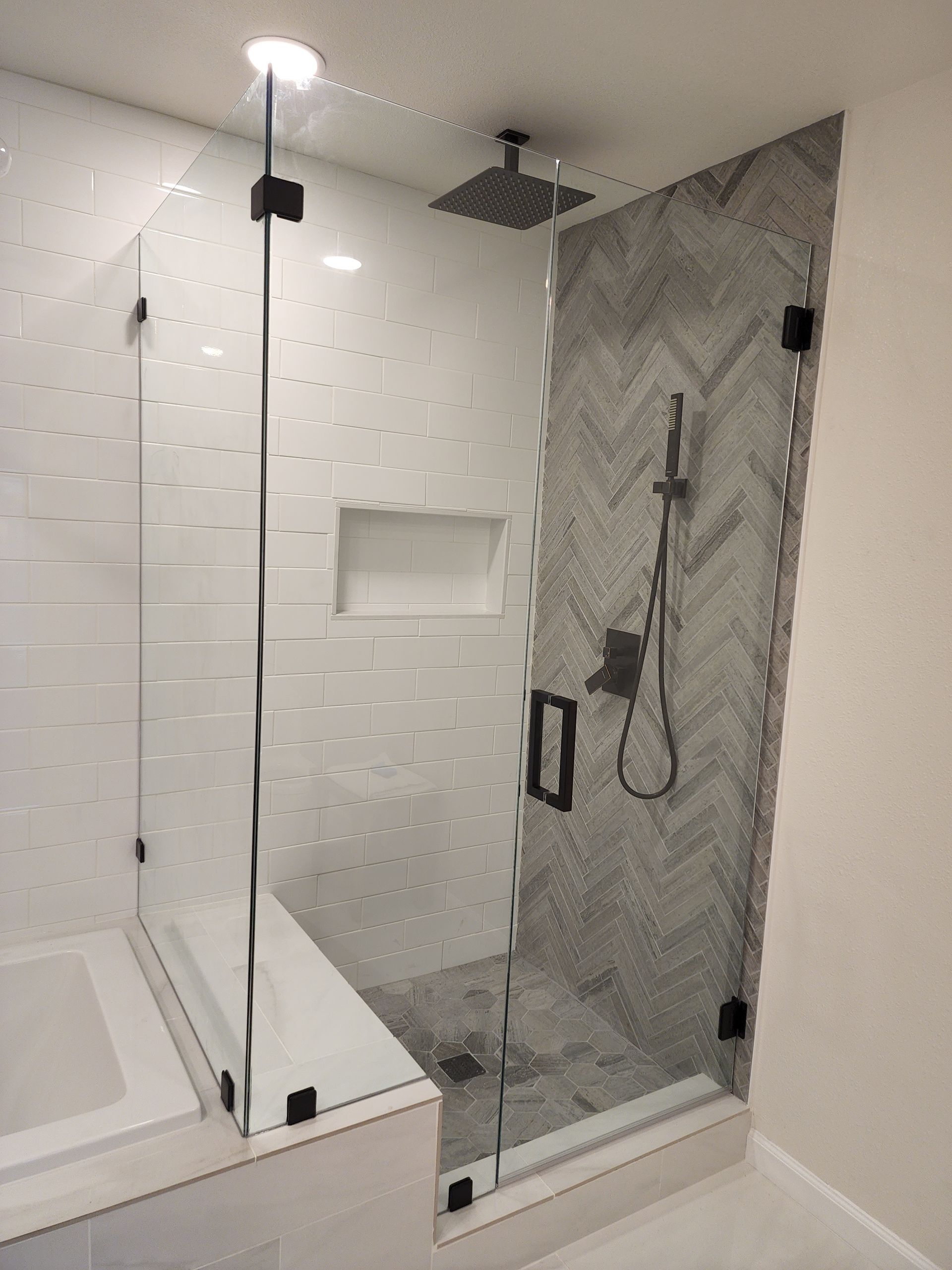 A walk-in shower with white horizontal tiles, a grey herringbone back wall, and a black-framed glass door.