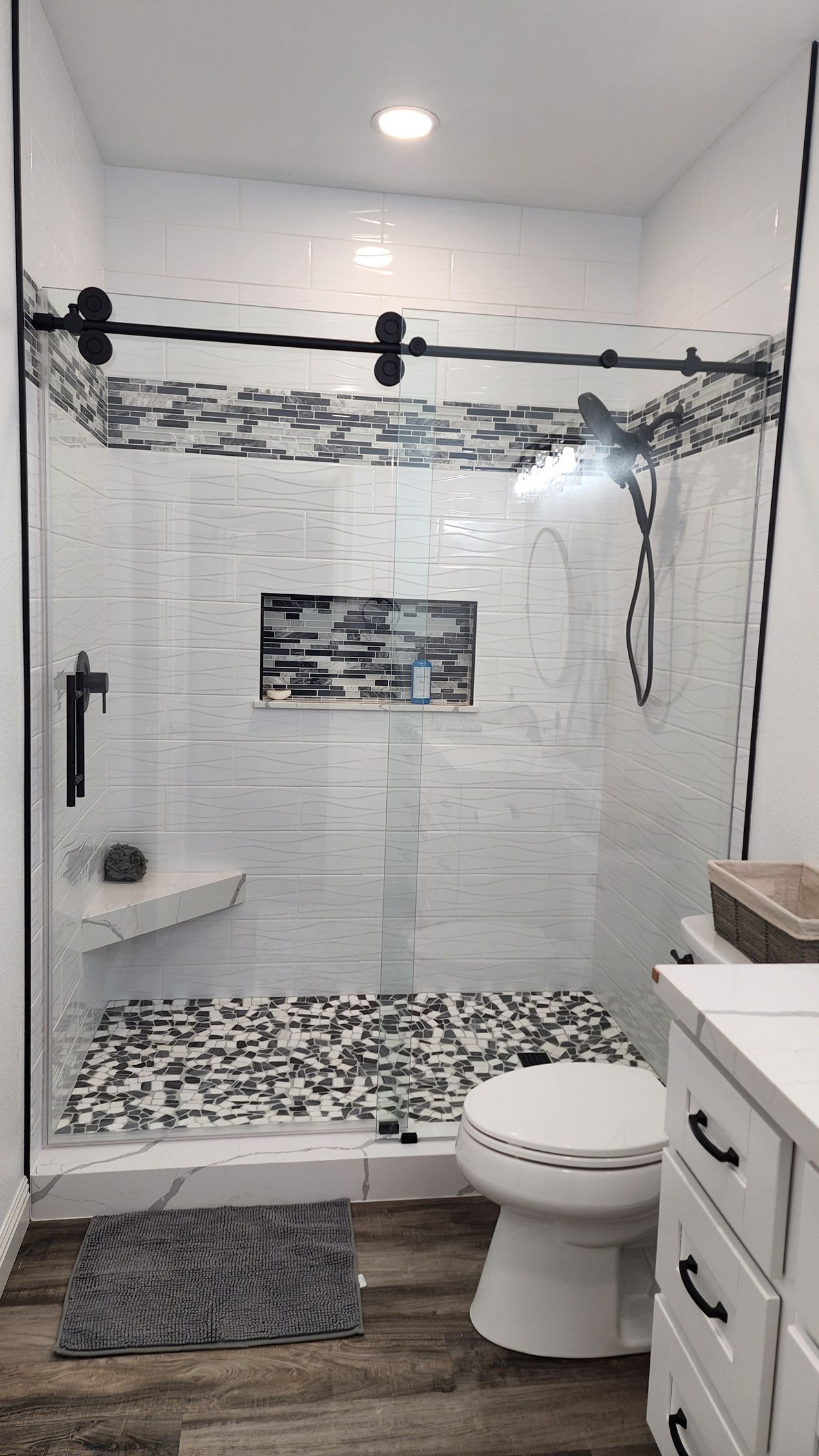 A modern bathroom featuring a glass-enclosed shower with black fixtures, a patterned tile floor, and white vanity cabinets.