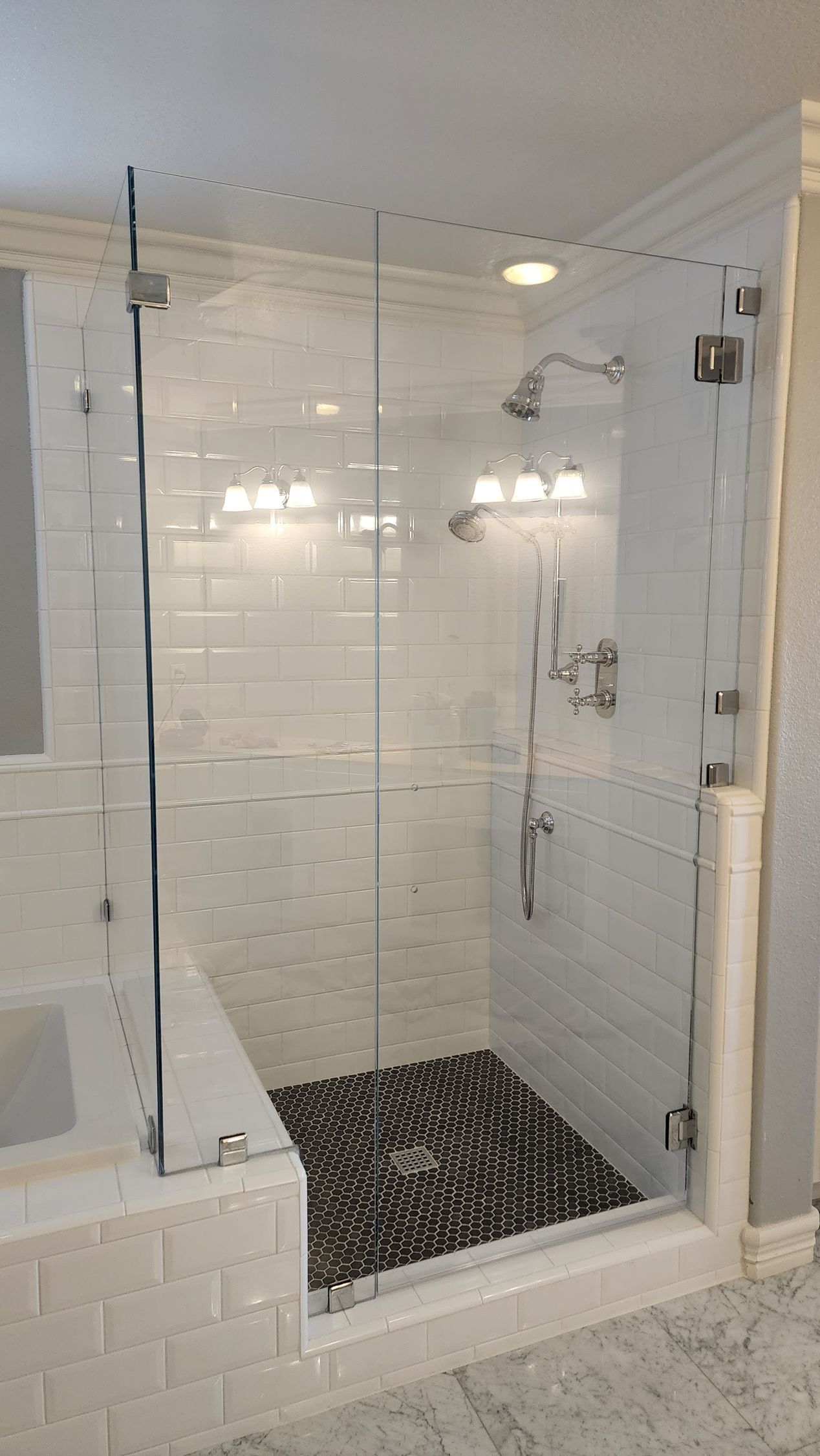 A tiled walk-in shower with a glass enclosure and a dark stone pebble floor.