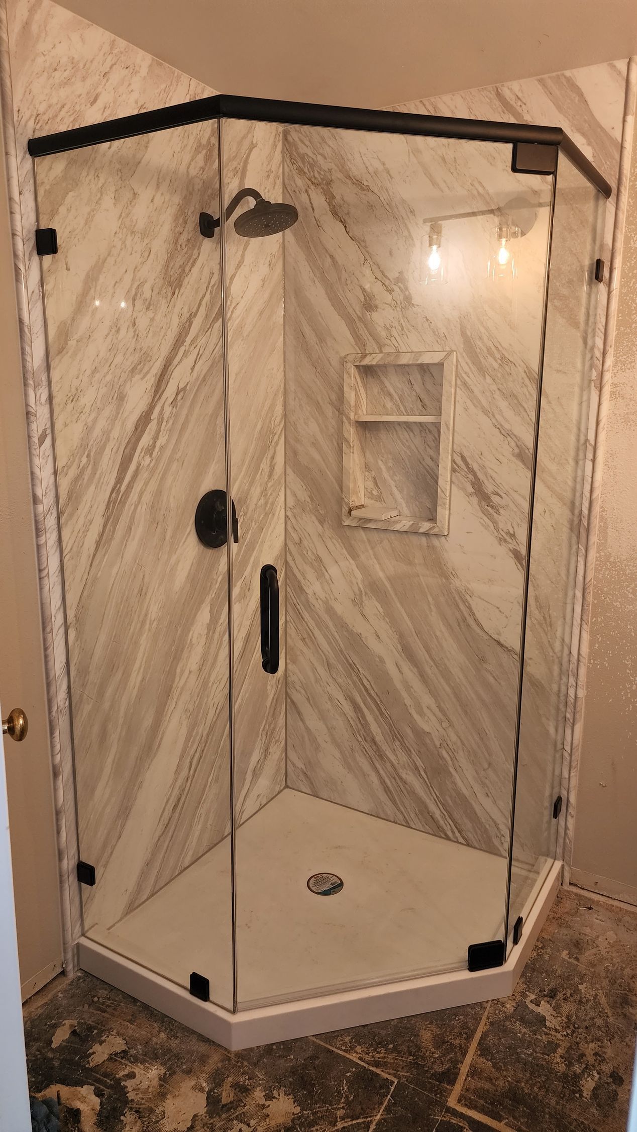 A glass corner shower stall with black frame, diagonal patterned tile walls, and a recessed shampoo niche.