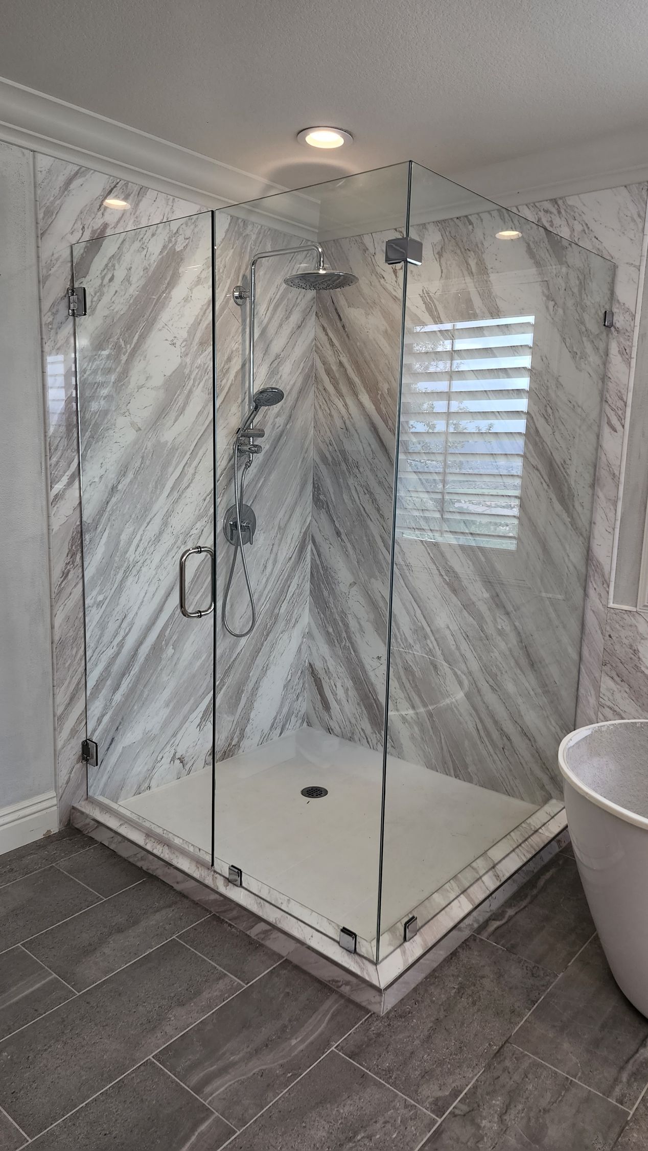 A frameless glass shower enclosure with diagonal marble-patterned tile walls and a white base in a modern bathroom.