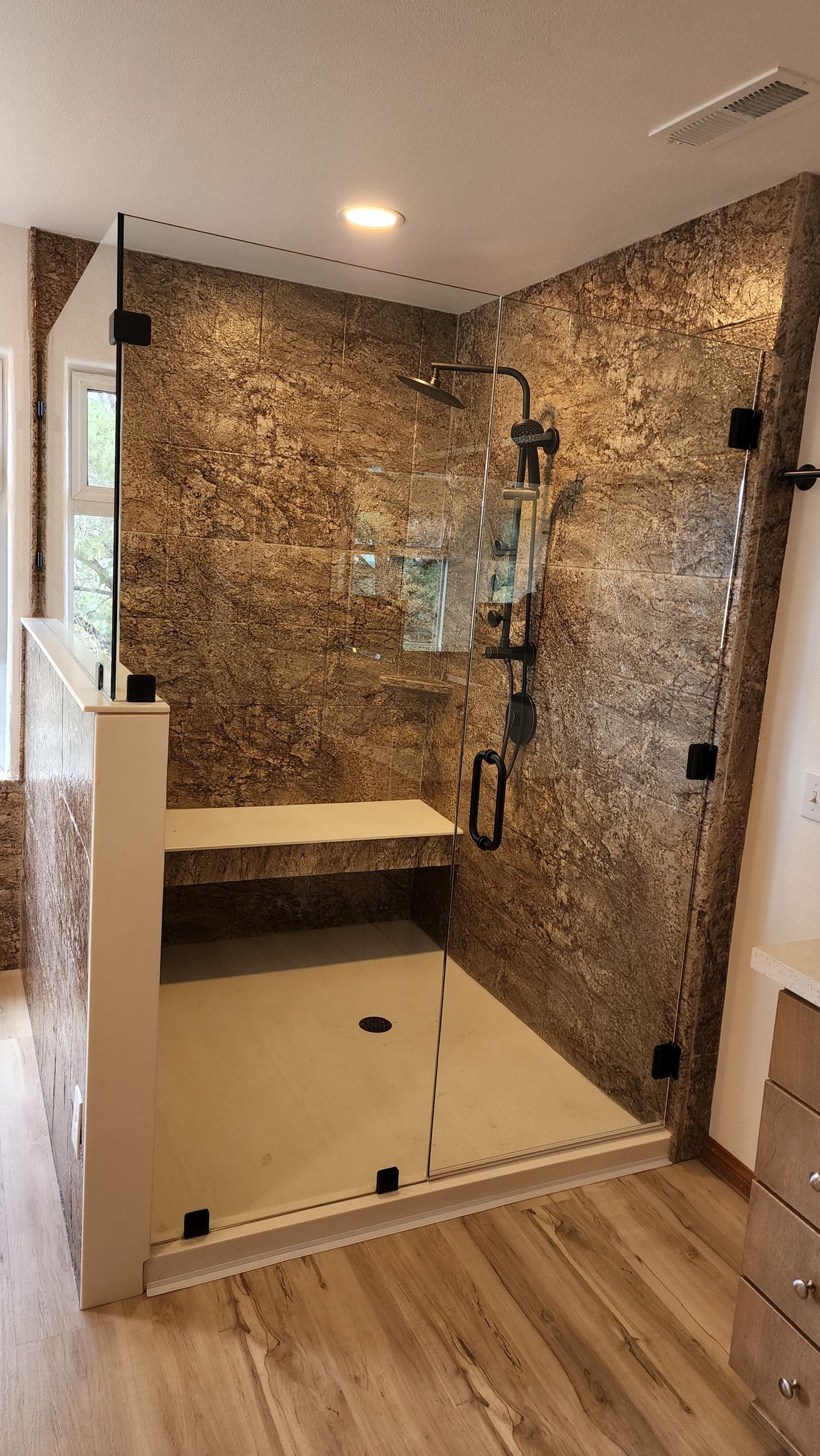 Modern shower with textured stone-patterned walls, a glass door, a built-in bench, and a white shower floor base.