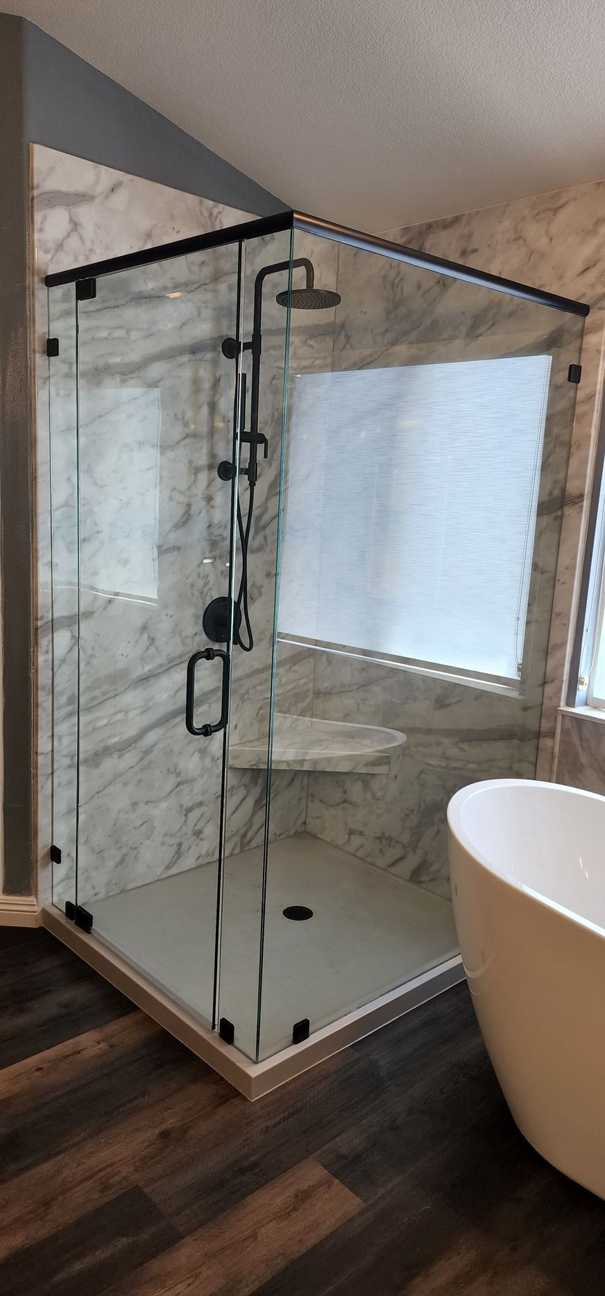 A modern, glass-enclosed corner shower with marble-look walls, matte black fixtures, and a built-in bench in a bathroom.