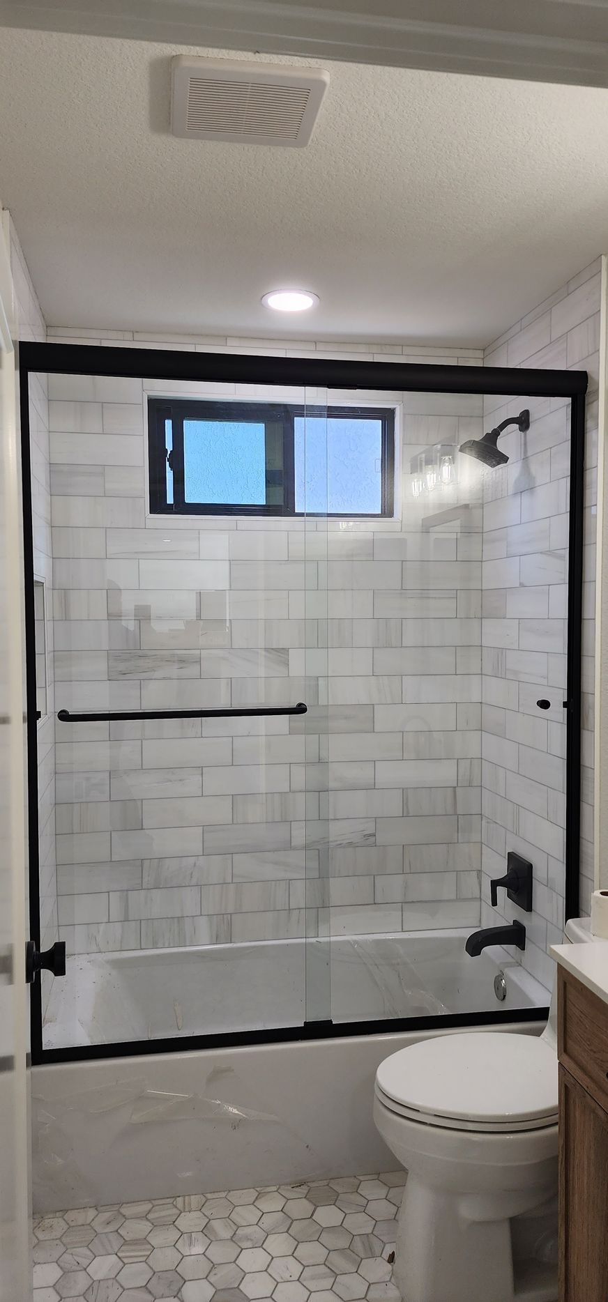 A modern bathroom with a glass shower enclosure, black trim, white subway tile walls, and a light-colored tile floor.
