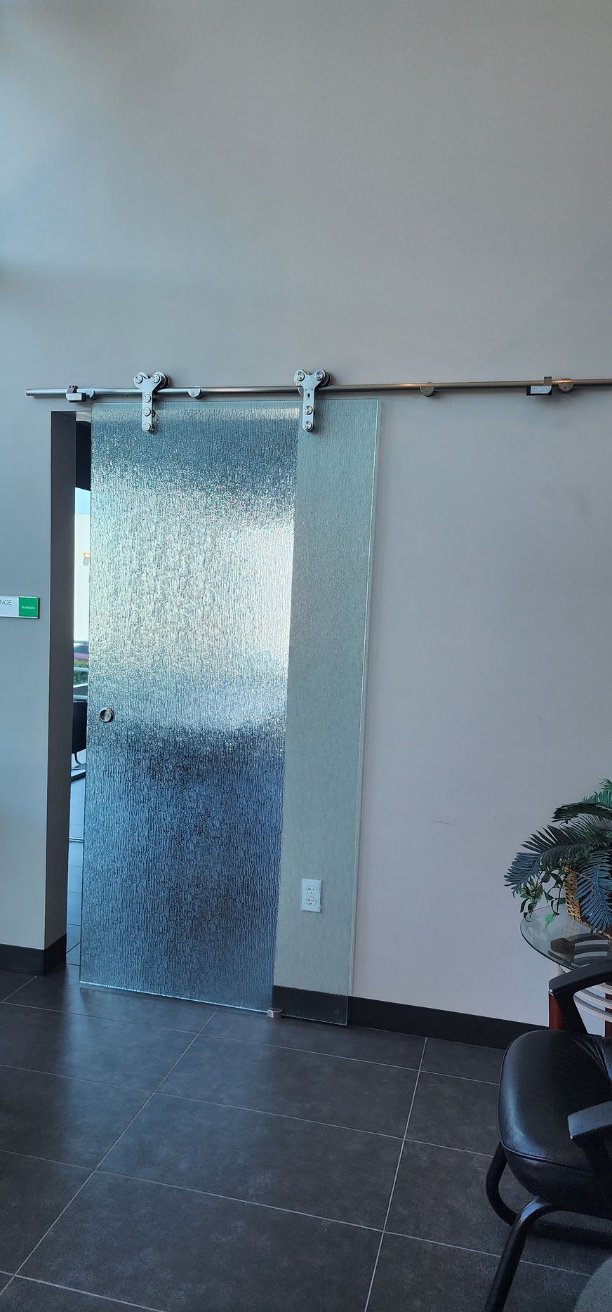 A sliding glass door with a decorative, textured pattern hanging on a metal track against a plain wall.