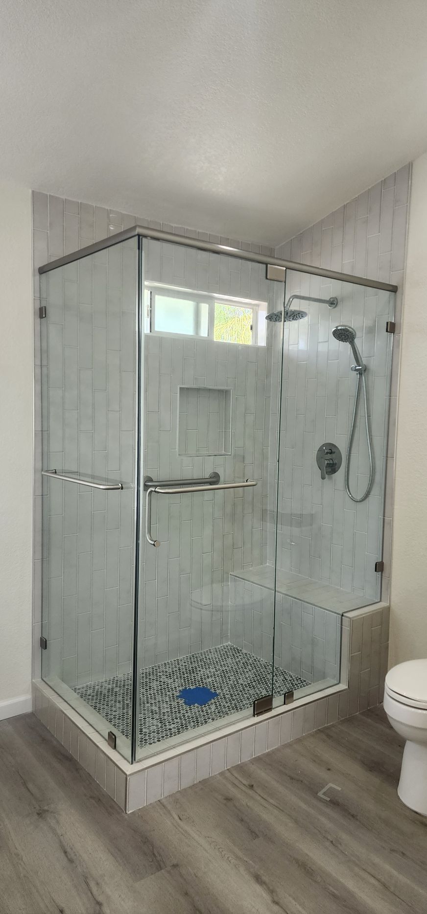 A modern walk-in shower with glass panels, light-colored tile walls, a pebble-stone floor, and a polished metal showerhead.