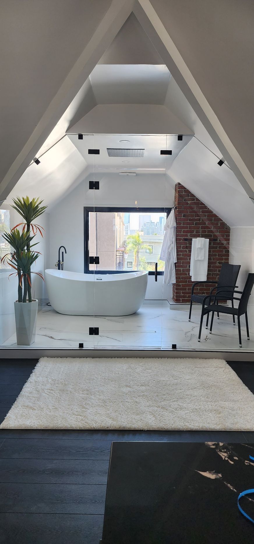 A modern bathroom with a white soaking tub, marble flooring, and a glass partition, set under an angled ceiling.